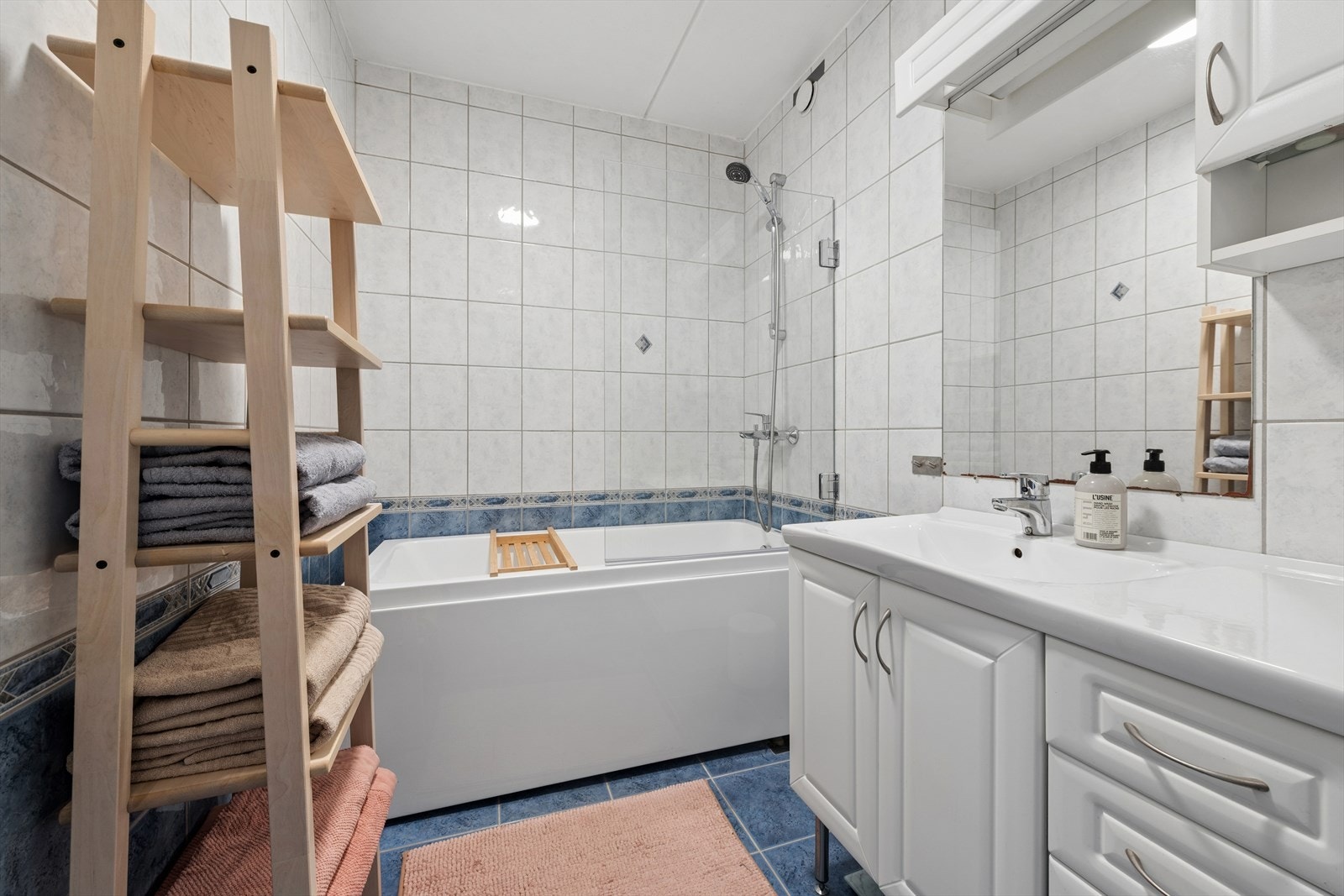 Badet har flislagte vegger og gulv, innredning med glatte fronter og nedsenket servant samt badekar med dusjvegg. Galleribilde