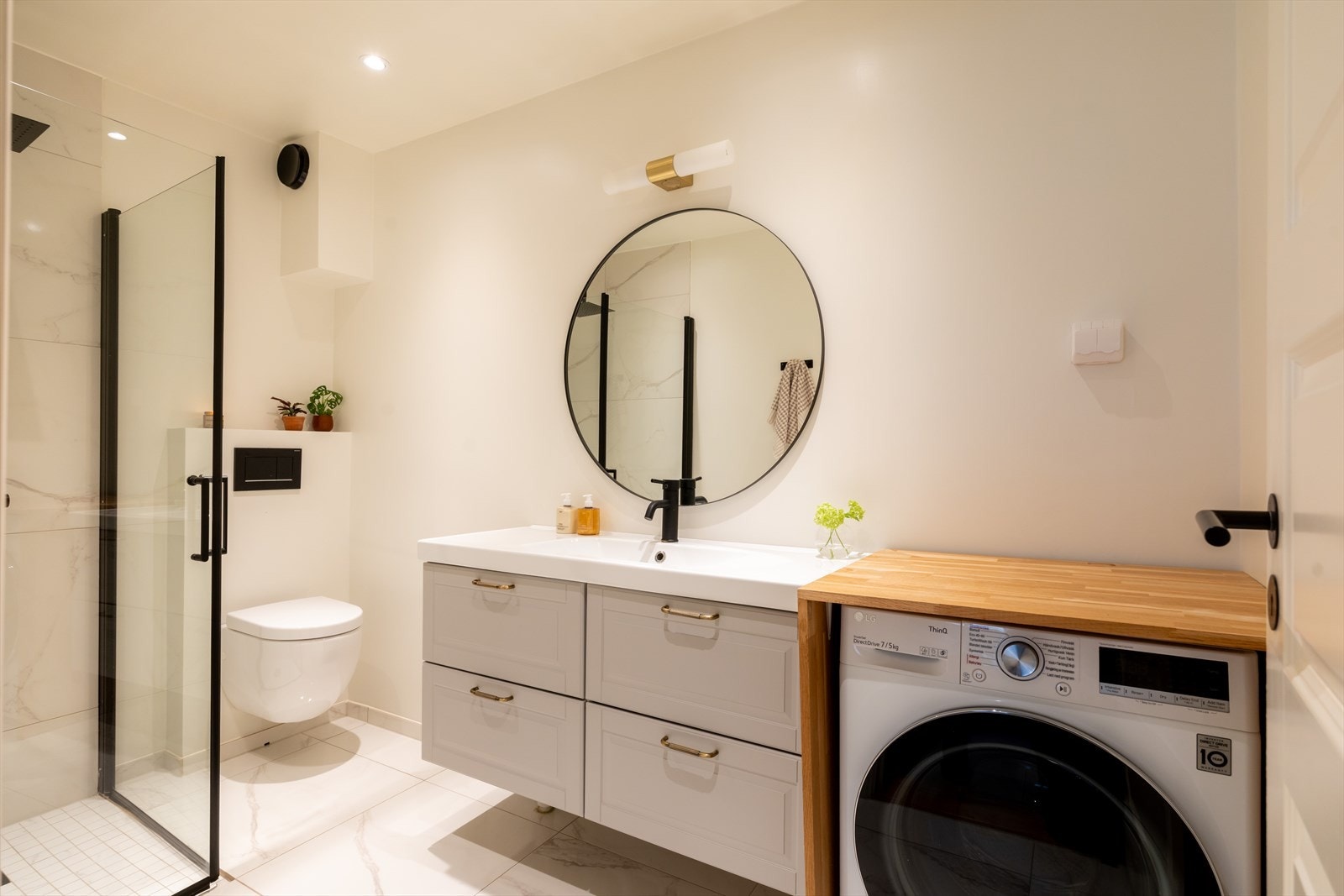 Delikat og moderne bad fra 2021 med stilrene overflater, god oppbevaringsplass og praktisk løsning med dusjhjørne og opplegg for vaskemaskin Galleribilde