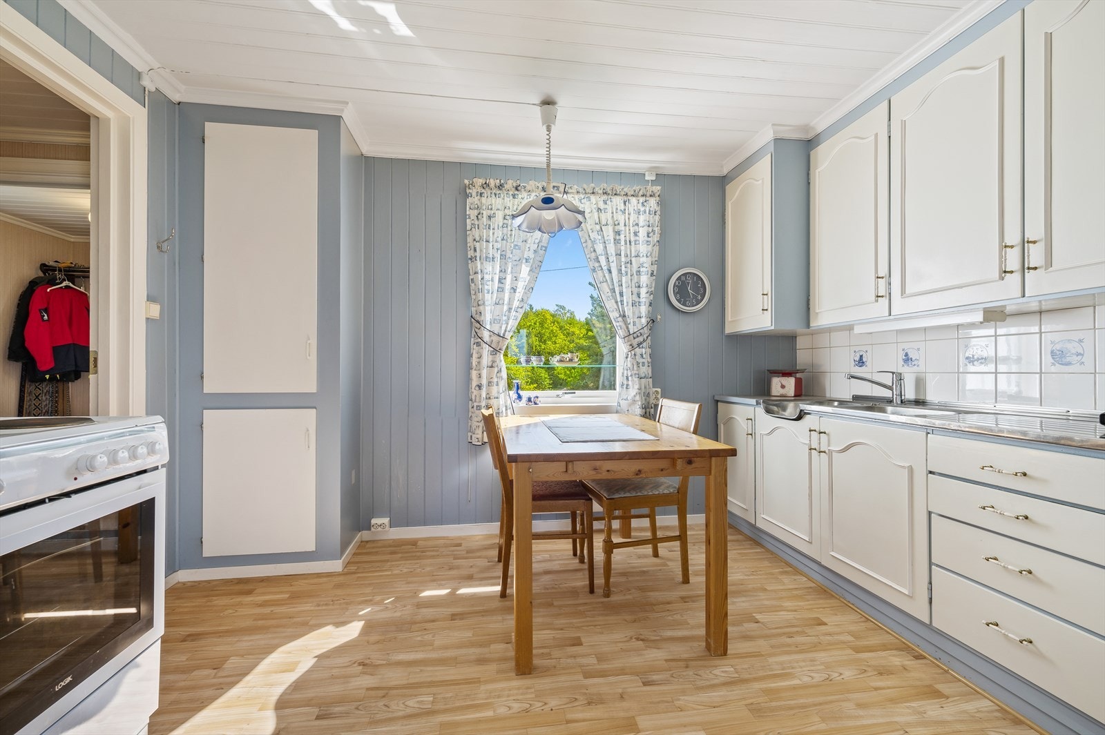 Kjøkkenet har en eldre, plassbygd innredning med profilerte fronter, stålbenk og frittstående hvitevarer (komfyr og kjøleskap). Galleribilde