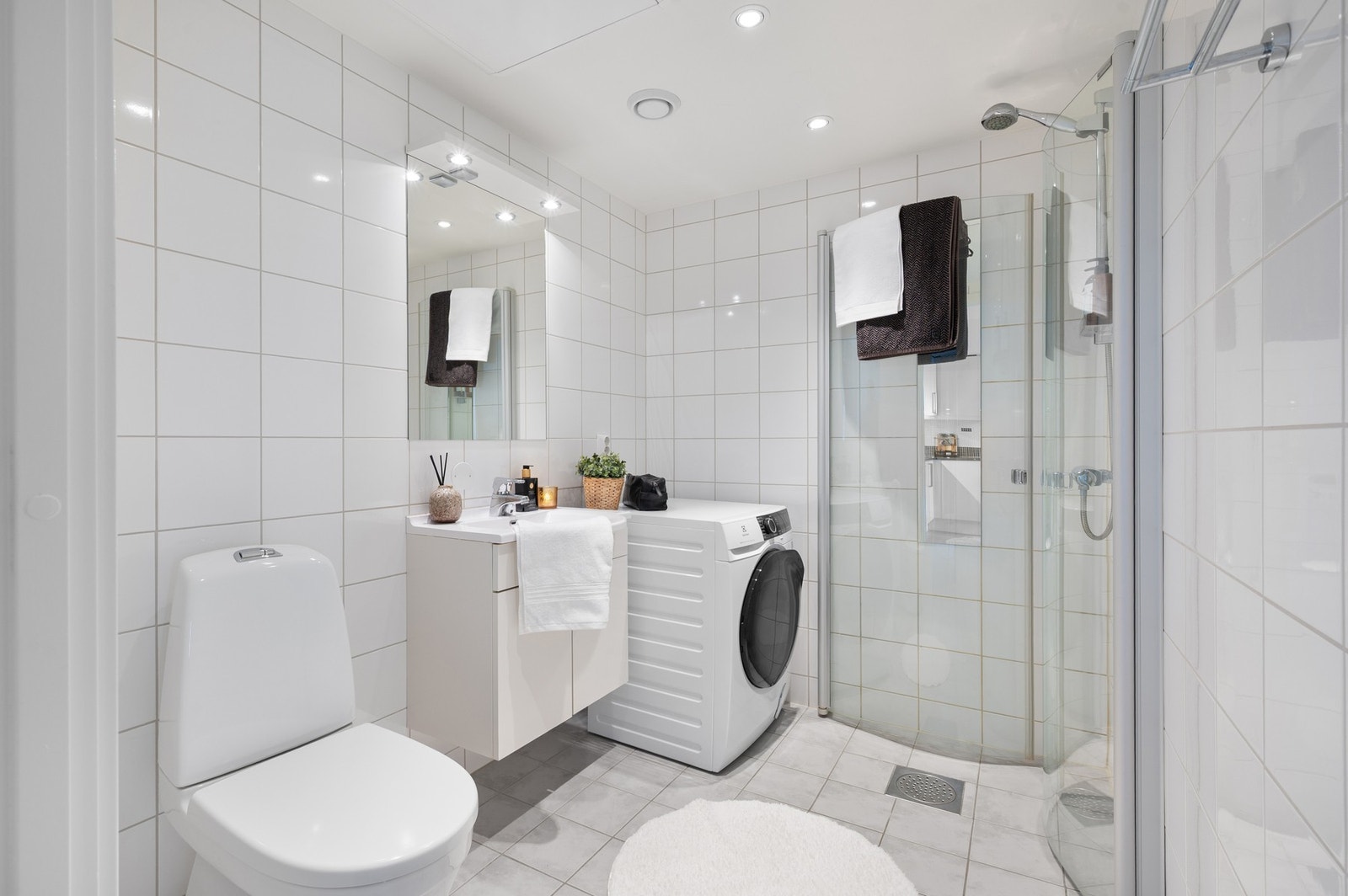 Lyst baderom med dusjhjørne, opplegg for vaskemaskin og praktisk innredning med servant og underskap. Galleribilde