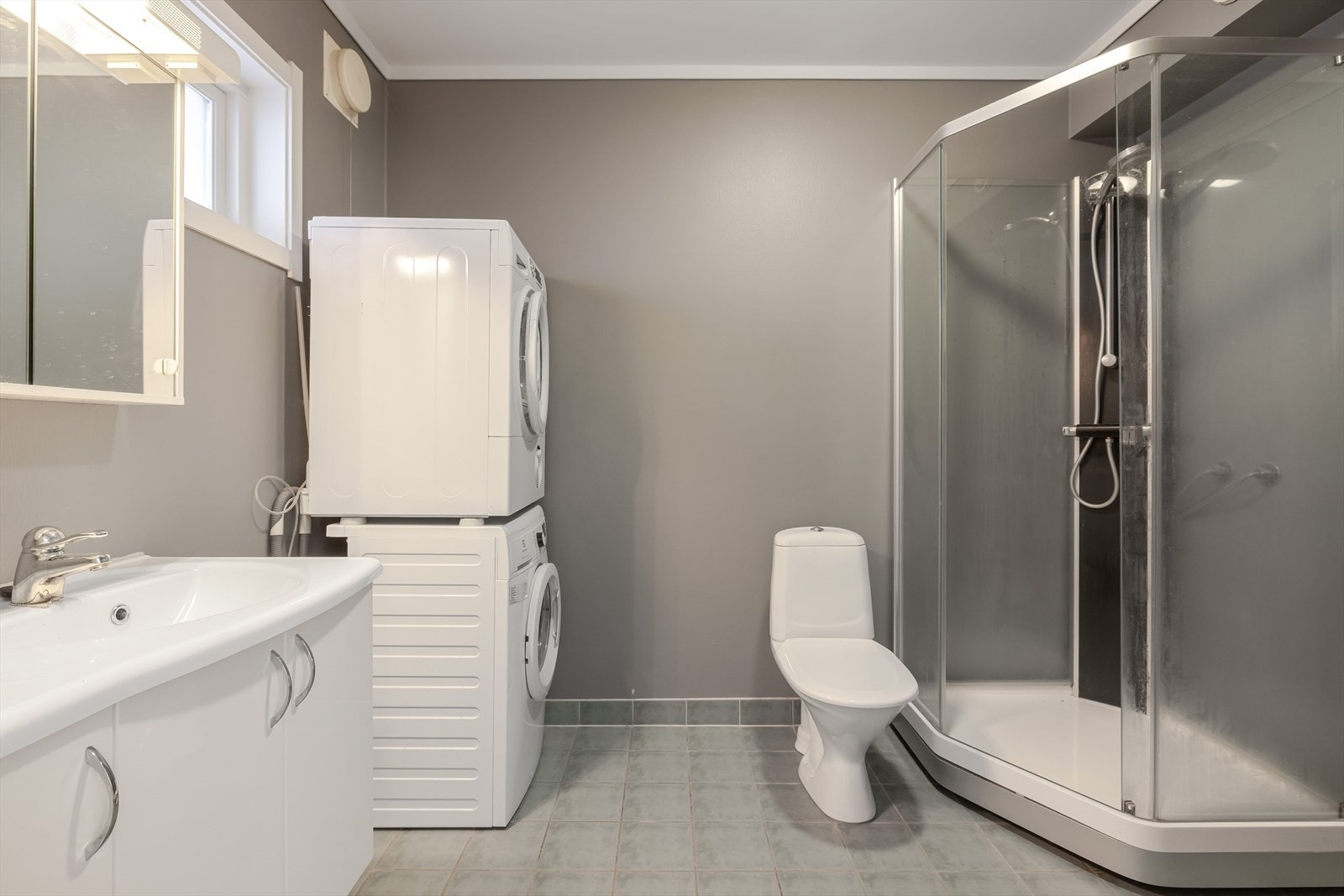 Baderomsinnredning med skap og heldekkende servant. I overkant av servanten er det speilskap med lys og elektrisk uttak. Det er opplegg fro vaskemaskin på badet. Galleribilde