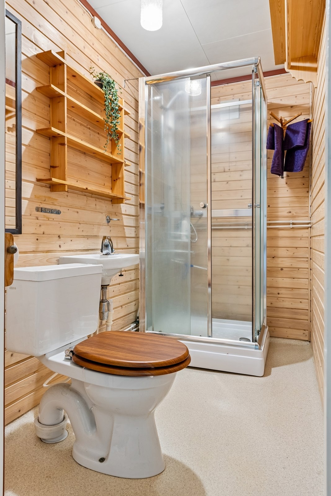 Bad i kjeller med gulvmontert WC, servant og dusjkabinett. Gulvet ble oppbygget med belegg og plater i 2000. Galleribilde