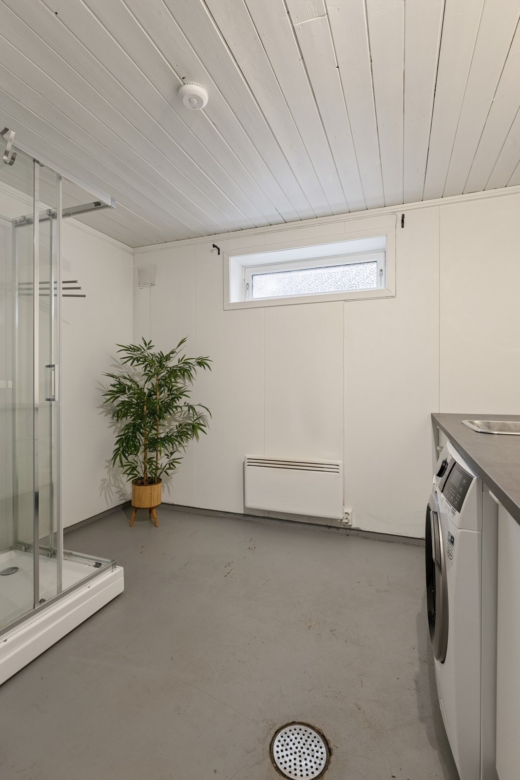 Vaskerom med malt betong på gulv, innredet med servant med underskap, speil, dusjkabinett og gulvmontert toalett. Galleribilde