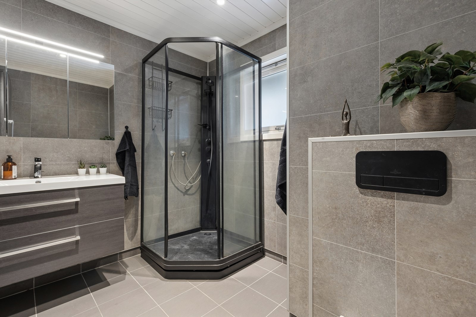 Delikat bad med våtromsplater på veggene og fliser på gulv med gulvvarme. Badet er innredet med servant med underskap, speilskap med tilhørende belysning, veggmontert toalett og dusjkabinett. Galleribilde