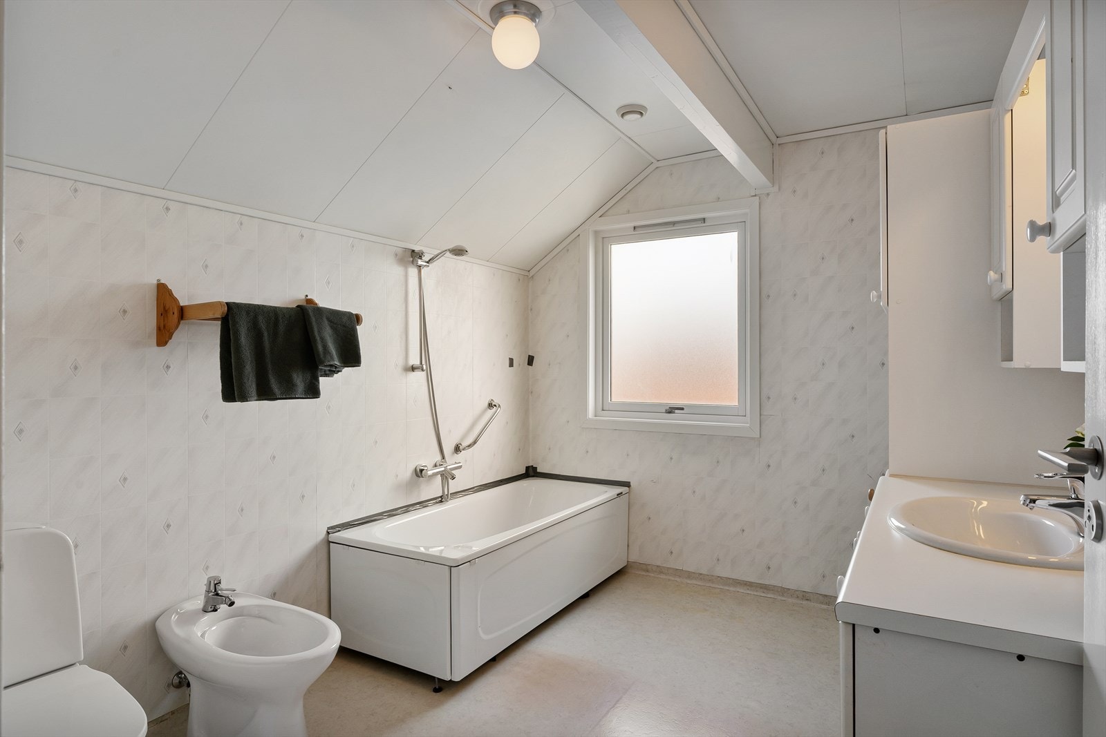 Bad med belegg på gulv og gulvvarme, innredet med wc, badekar og seksjon med vask Galleribilde