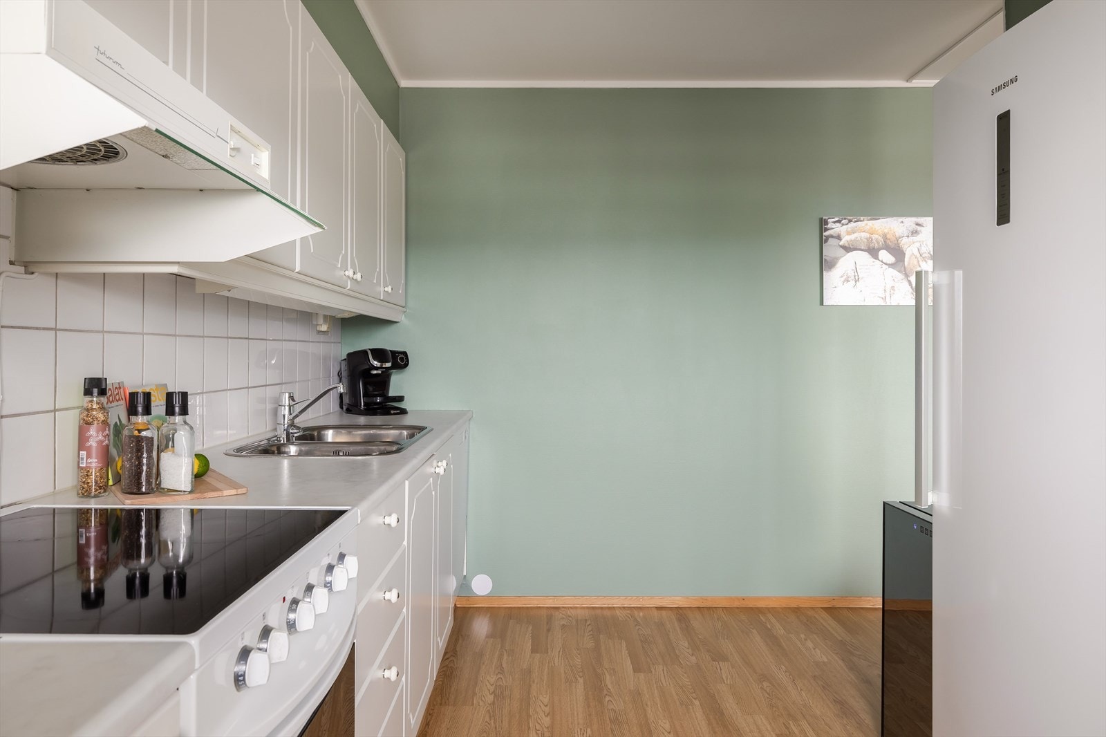 Innredningen har hvite, profilerte fronter og laminert benkeplate med dobbel oppvaskkum i rustfritt stål. Galleribilde