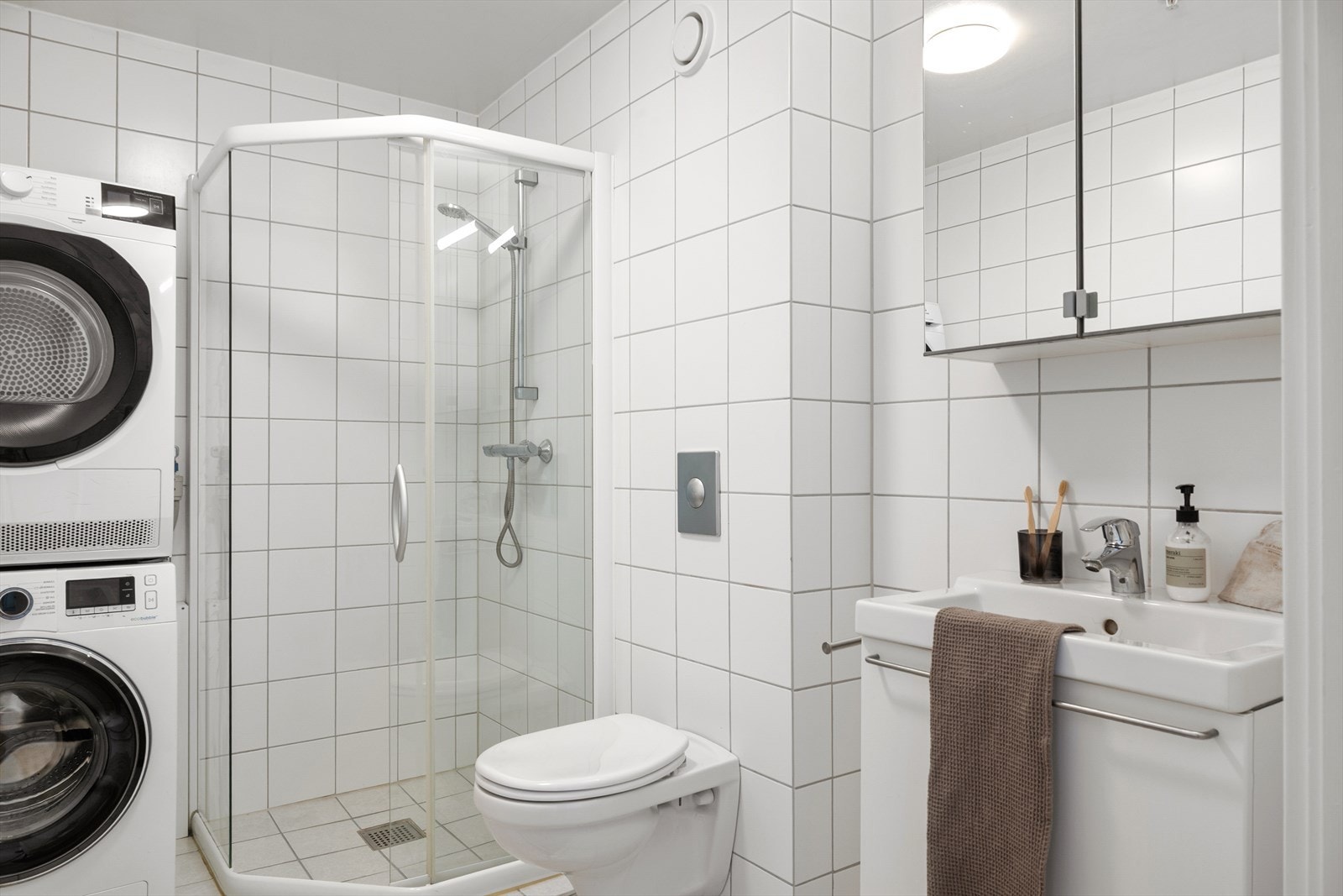 Badet er innredet med hvit servant med speil, vegghengt wc, dusjnisje med glassdører, samt opplegg for vaskemaskin og tørketrommel. Galleribilde