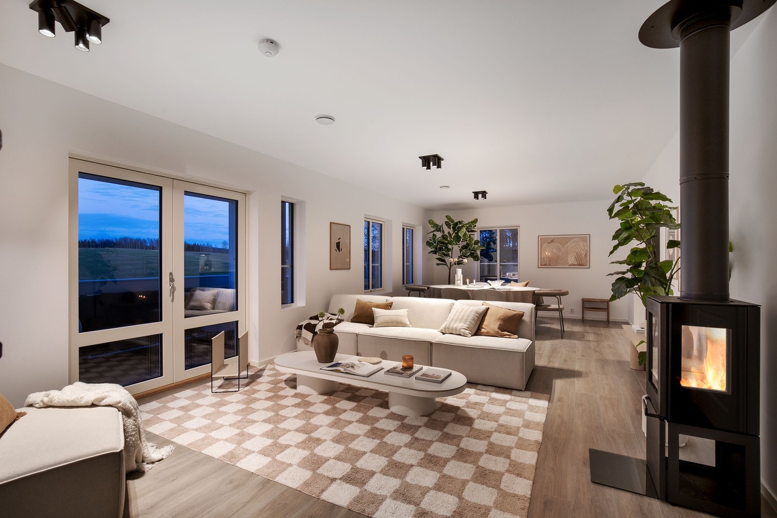 Lys og innbydende stue med store vindusflater, moderne peisovn og lyspigmentert laminat på gulv Galleribilde