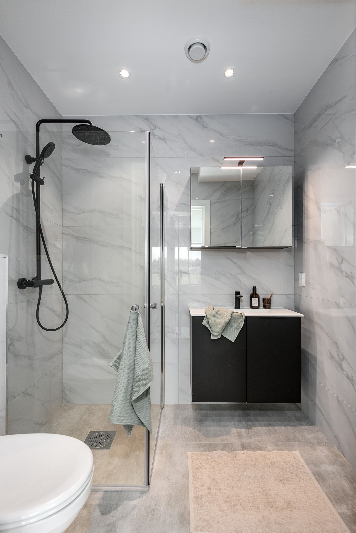 Delikat flislagt bad i 1. etasje med gulvvarme, servantmøbel, speilskap, vegghengt toalett og dusjhjørne med glassdører og regnfallsdusj. Galleribilde