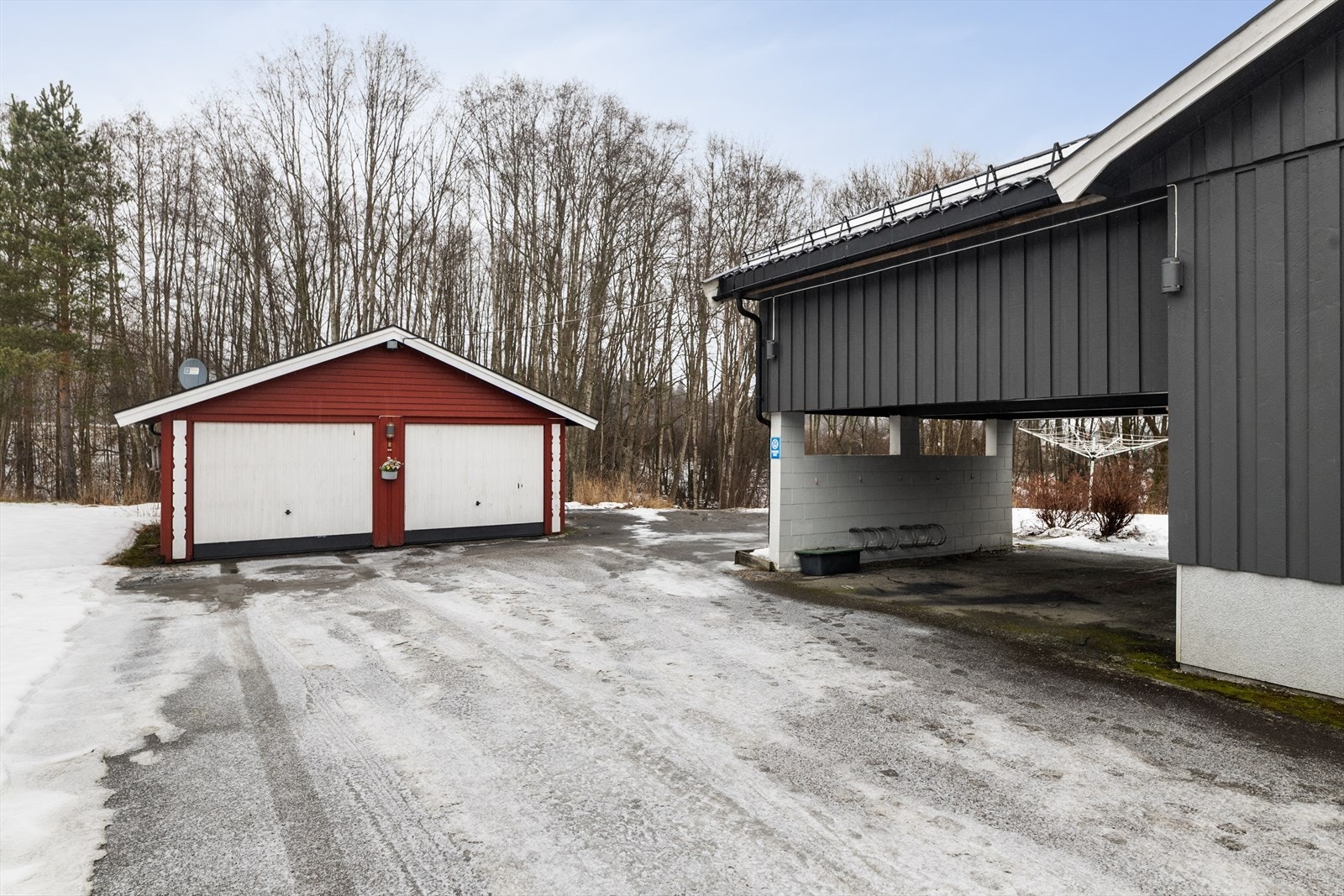 Stor, gruset gårdsplass med biloppstillingsplasser og carport, samt dobbeltgarasje med vippeporter og ladepunkt for elbil. Galleribilde