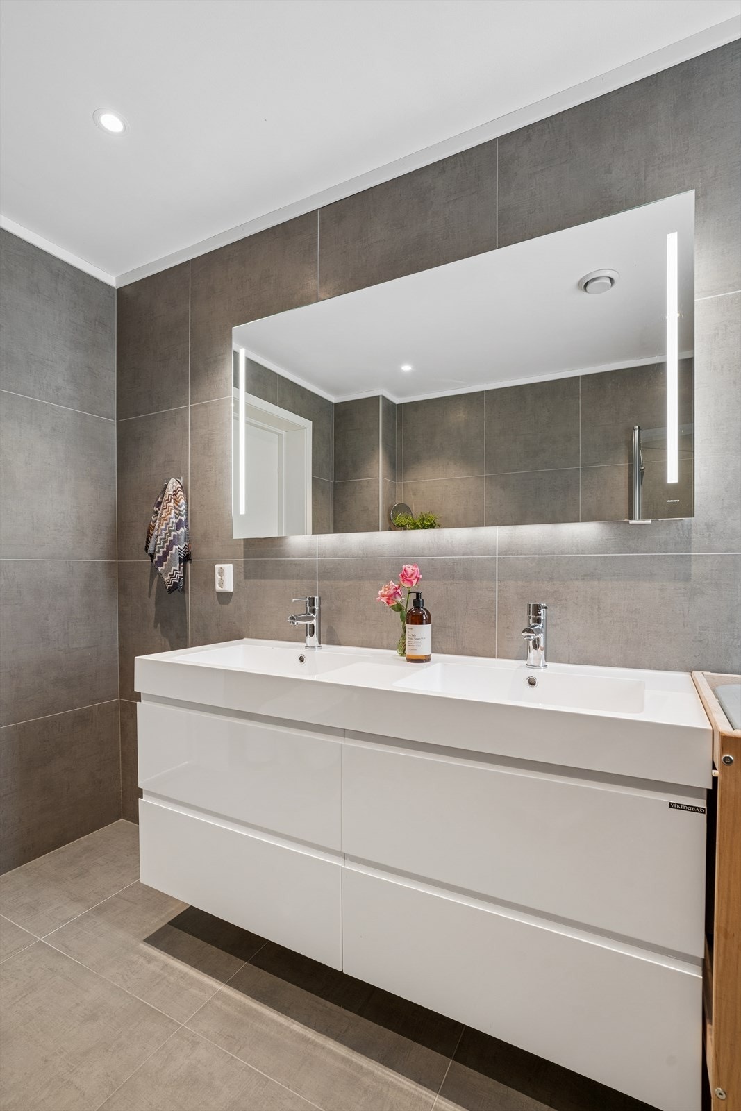 Badet er innredet med baderomsmøbel med heldekkende dobbel servant, speil med belysning, vegghengt toalett og dusjhjørne med innfellbare glassdører. Galleribilde