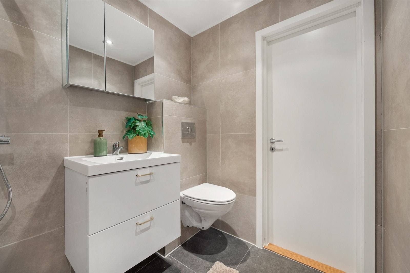 Badet er innredet med vegghengt toalett, servant med skuffeinnredning og speilskap med belysning. Galleribilde