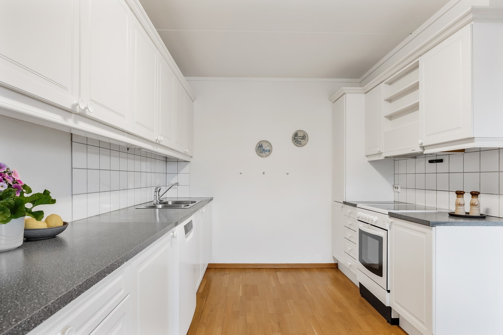 Innredningen består av to parallelle seksjoner og har hvite, profilerte fronter og grå laminatbenkeplate med dobbel oppvaskkum. Galleribilde