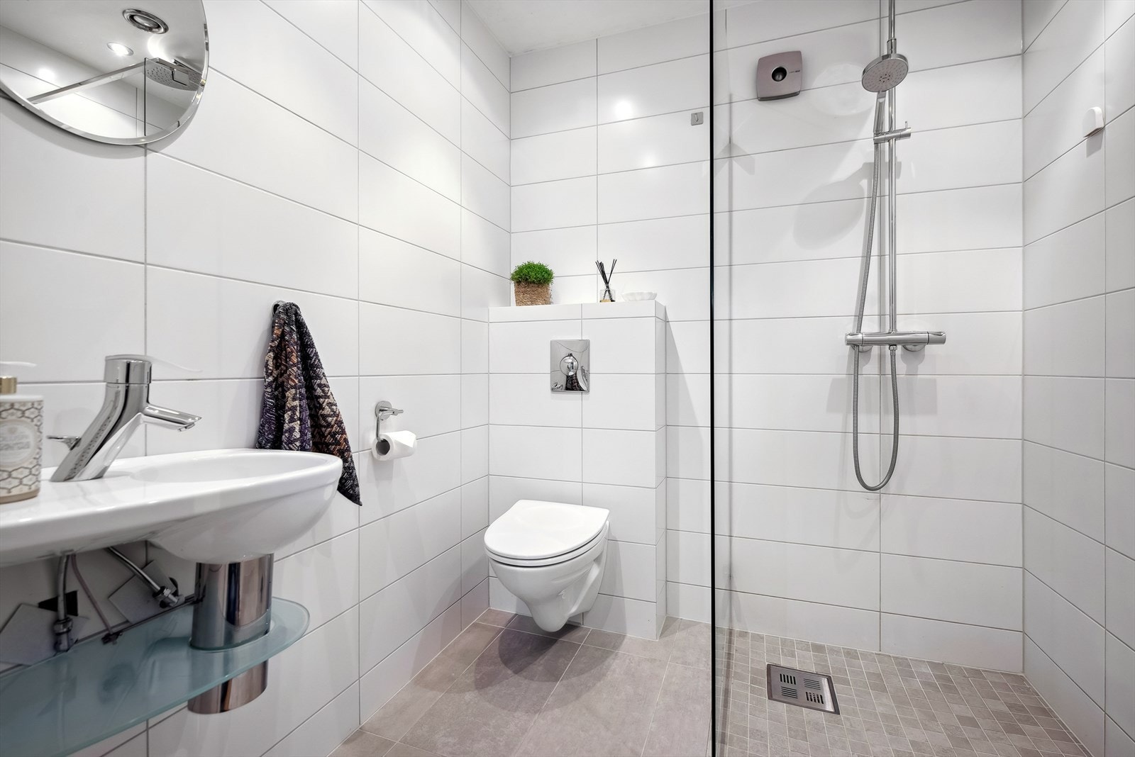 Badet fremstår lyst, moderne og stilrent med helflisede overflater, vegghengt toalett, servant og dusjløsning med glassvegg. Galleribilde