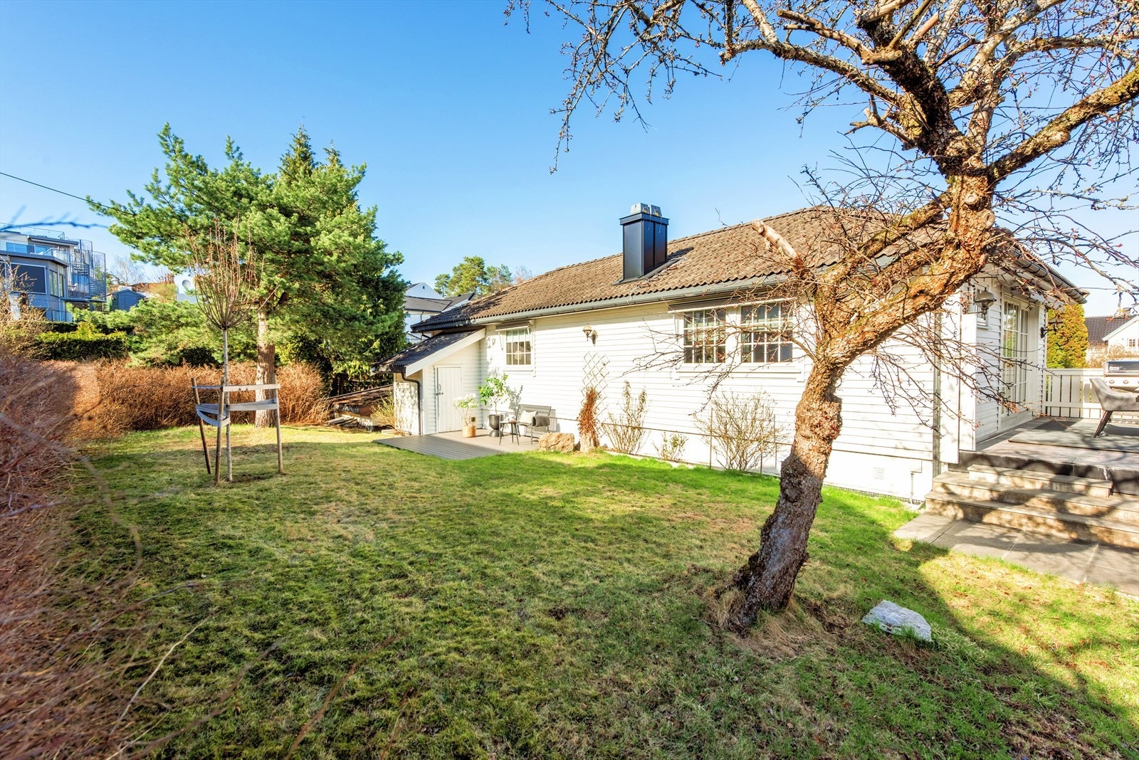 Skjermet og hyggelig hageområde med plen, beplantning og terrasse langs boligen. Her får du en fin kombinasjon av grønt uterom og gode oppholdssoner tett på huset. Galleribilde