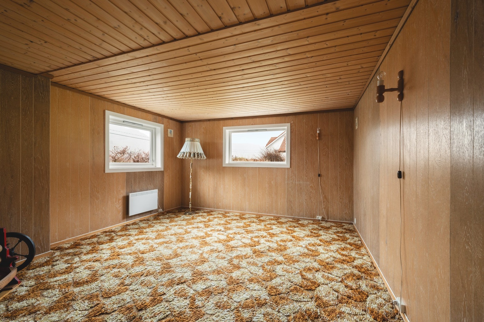 Kjellerstue med finerplater på vegg og heldekkende teppe. Galleribilde