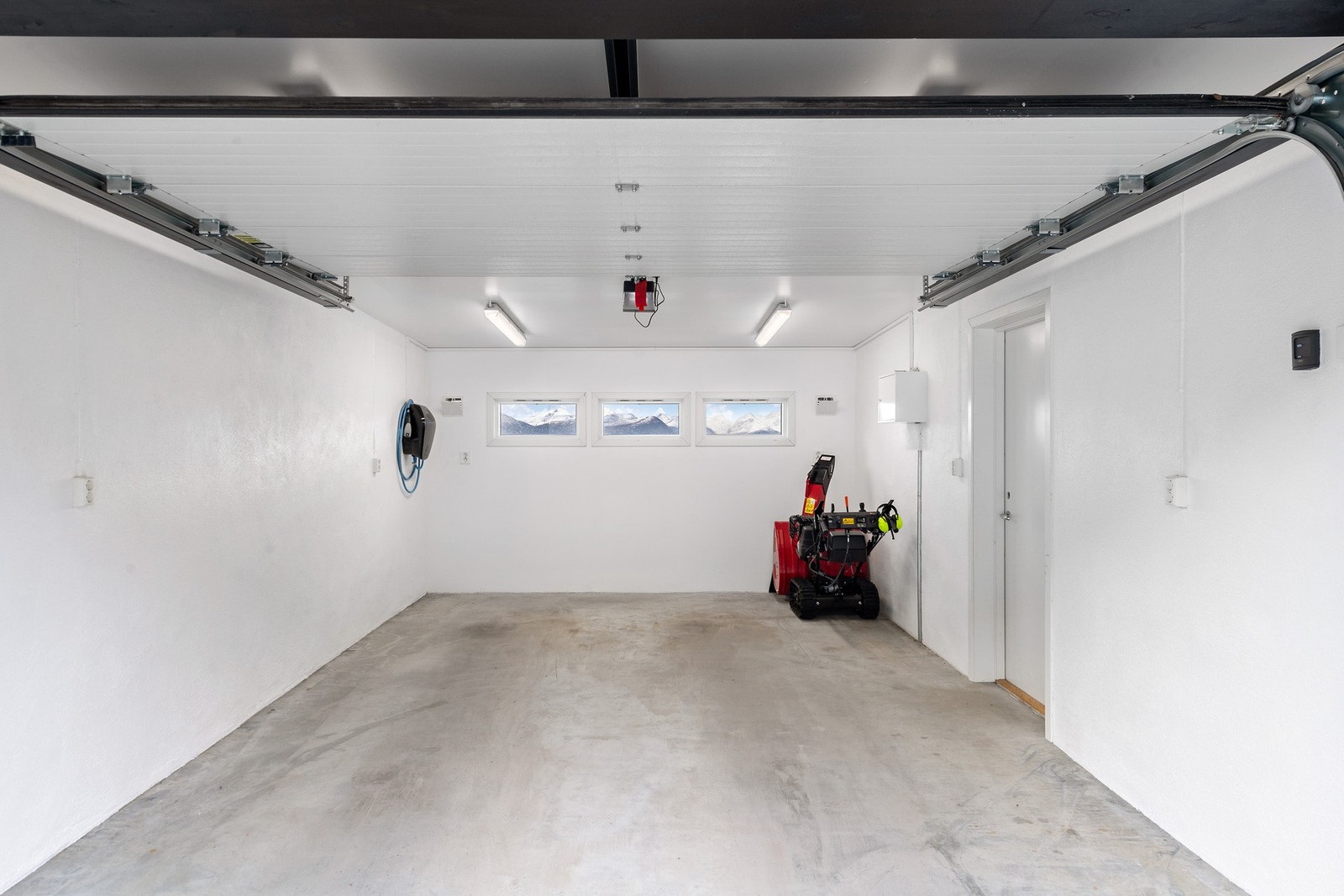 Eiendommen har 2 garasjer. Begge garasjer har elbillader. Dette er garasjen mot øst fra 2018. Her er det adkomst til boligen via takoverbygd svalgang. Galleribilde