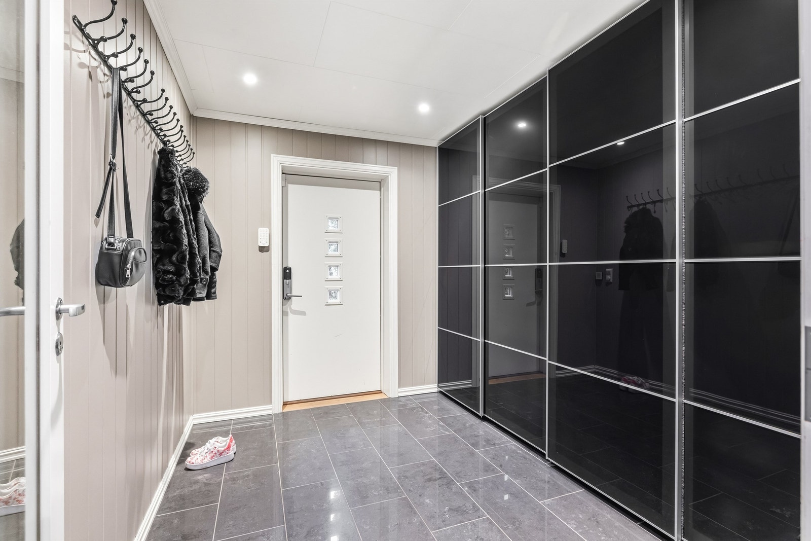 Romslig entré med mørke gulvfliser og gulvvarme. En bred skyvedørsgarderobe med sotede fronter gir utmerket oppbevaring. Galleribilde