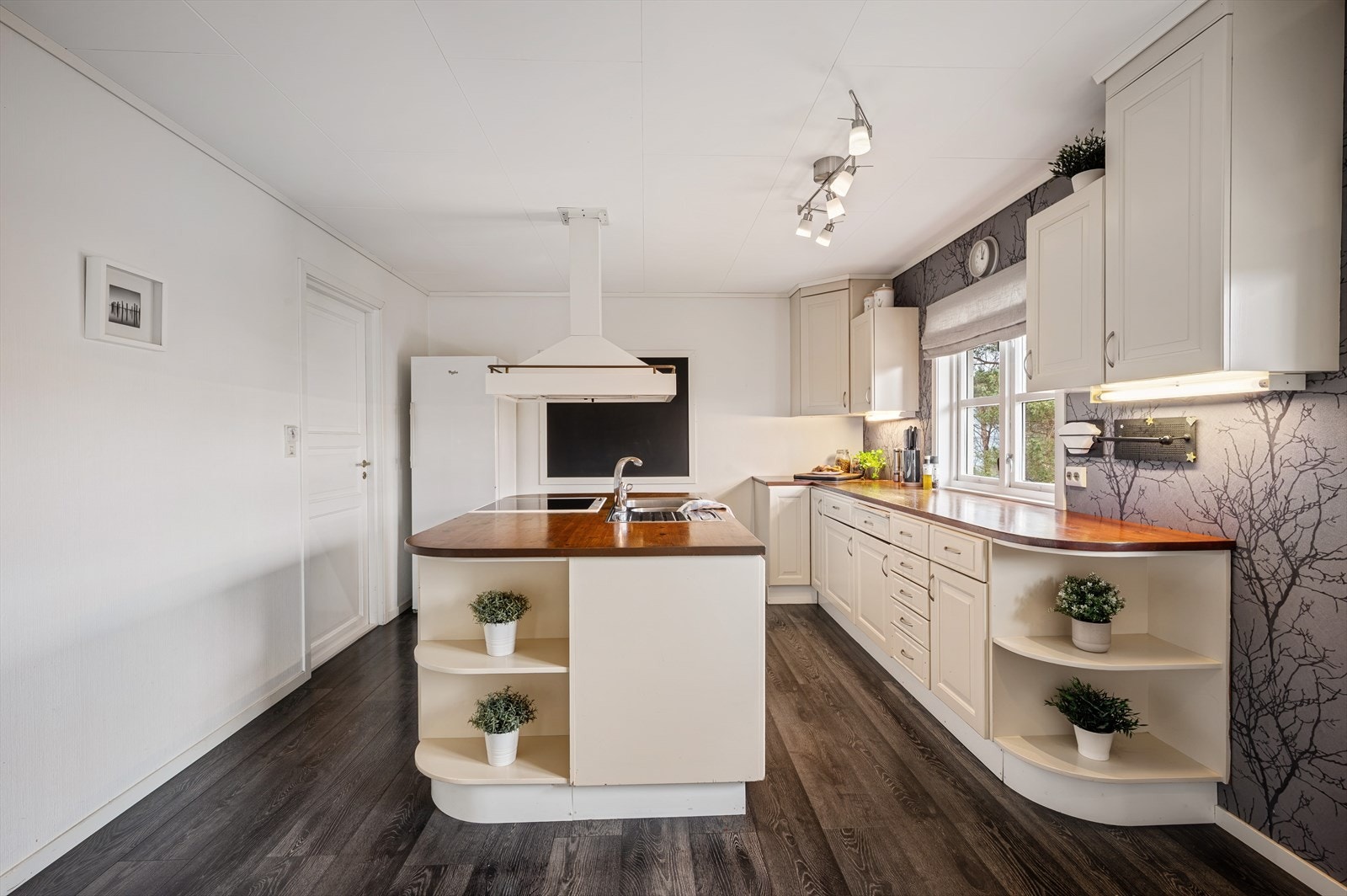 Ett innholdsrikt kjøkken i god størrelse. Kjøkkenet har profilerte fronter, benkeplate med nedfelt stålvask, komfyr, oppvaskmaskin og kjøleskap. Galleribilde