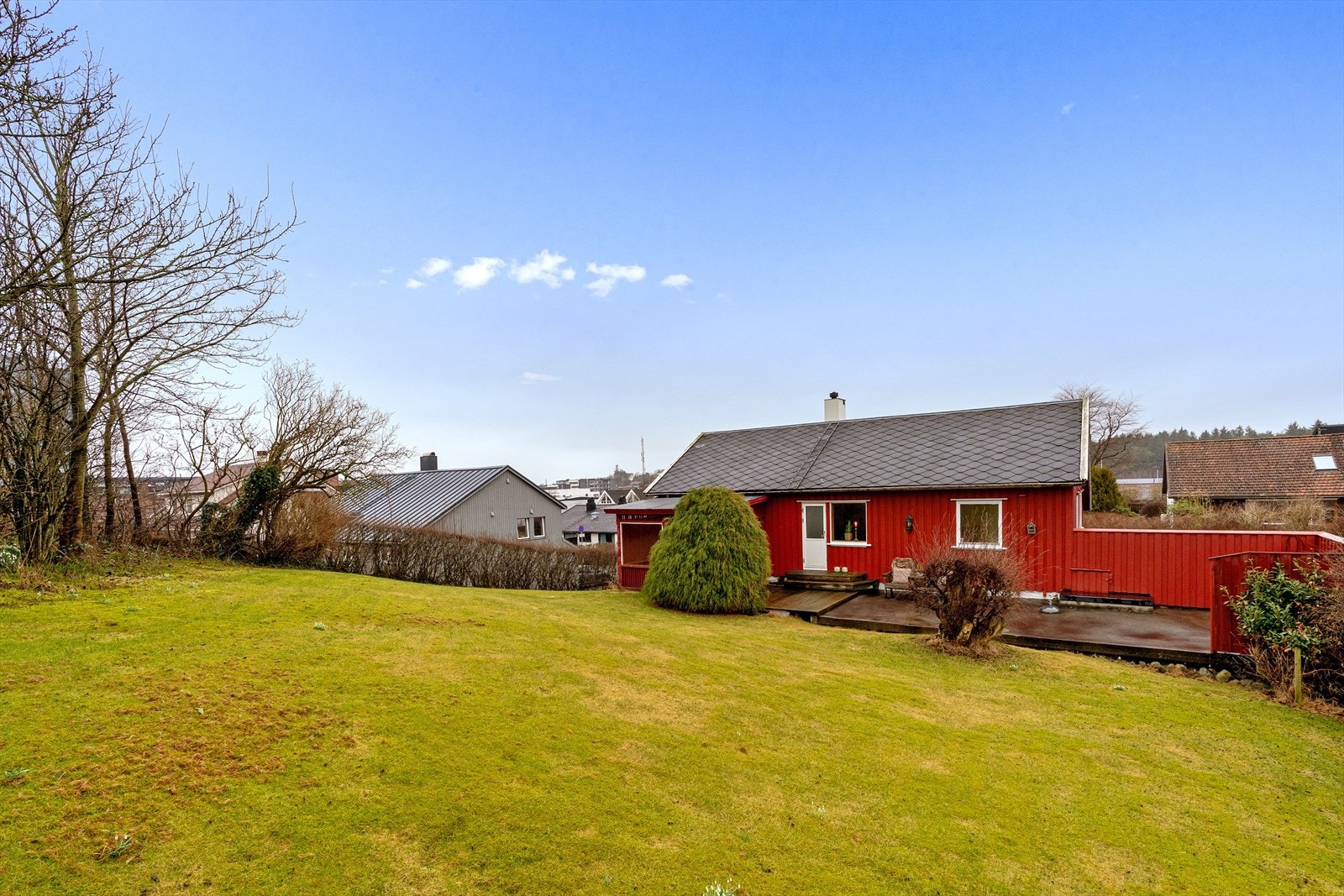 Tomten er lett skrånet. og har skjermet og stor gressplen på oppsiden av huset. Galleribilde