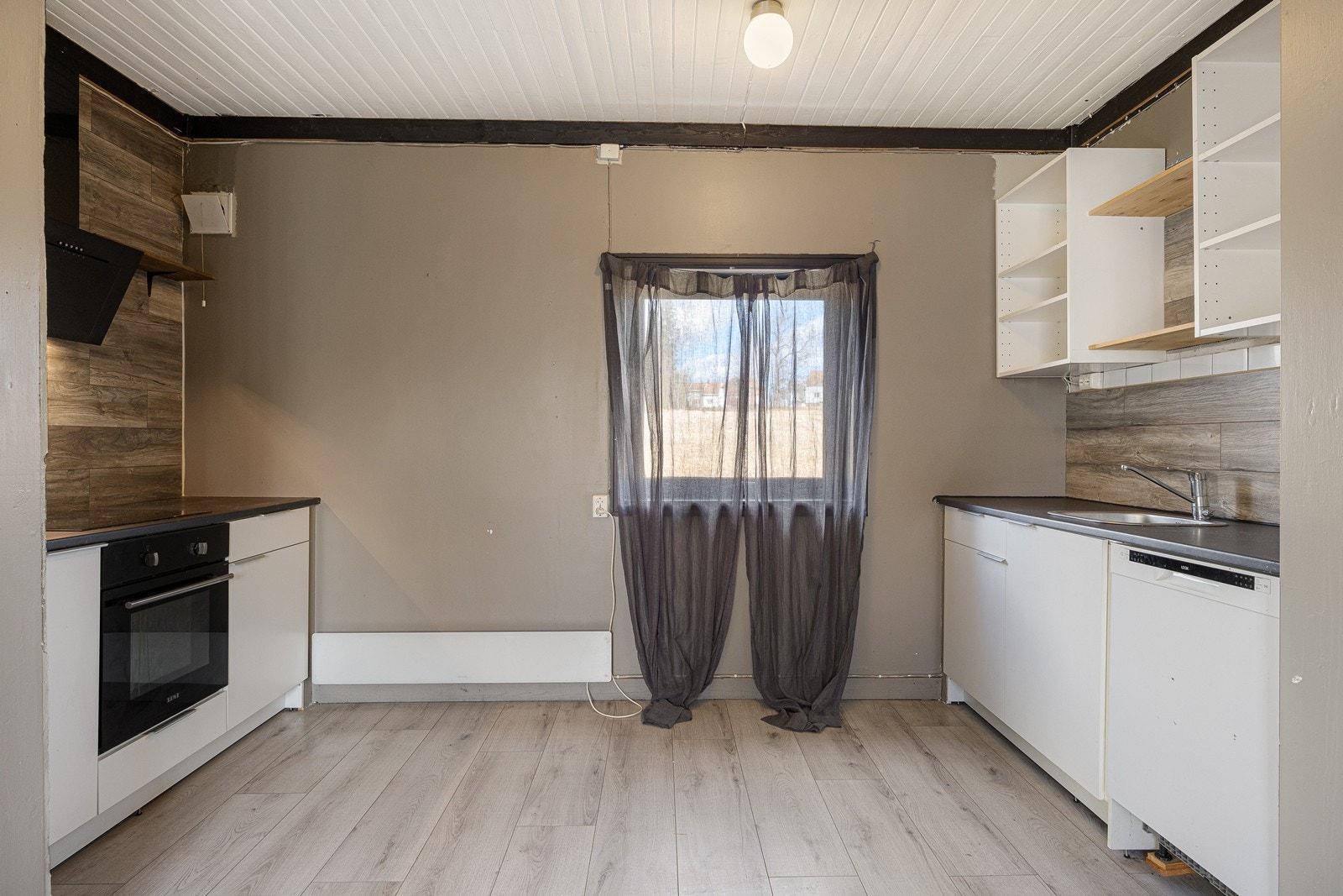 Kjøkkeninnredningen har hvite fronter og grå laminatbenkeplate med nedfelt kum i stål. Veggene over benkene er kledd med laminat. Galleribilde