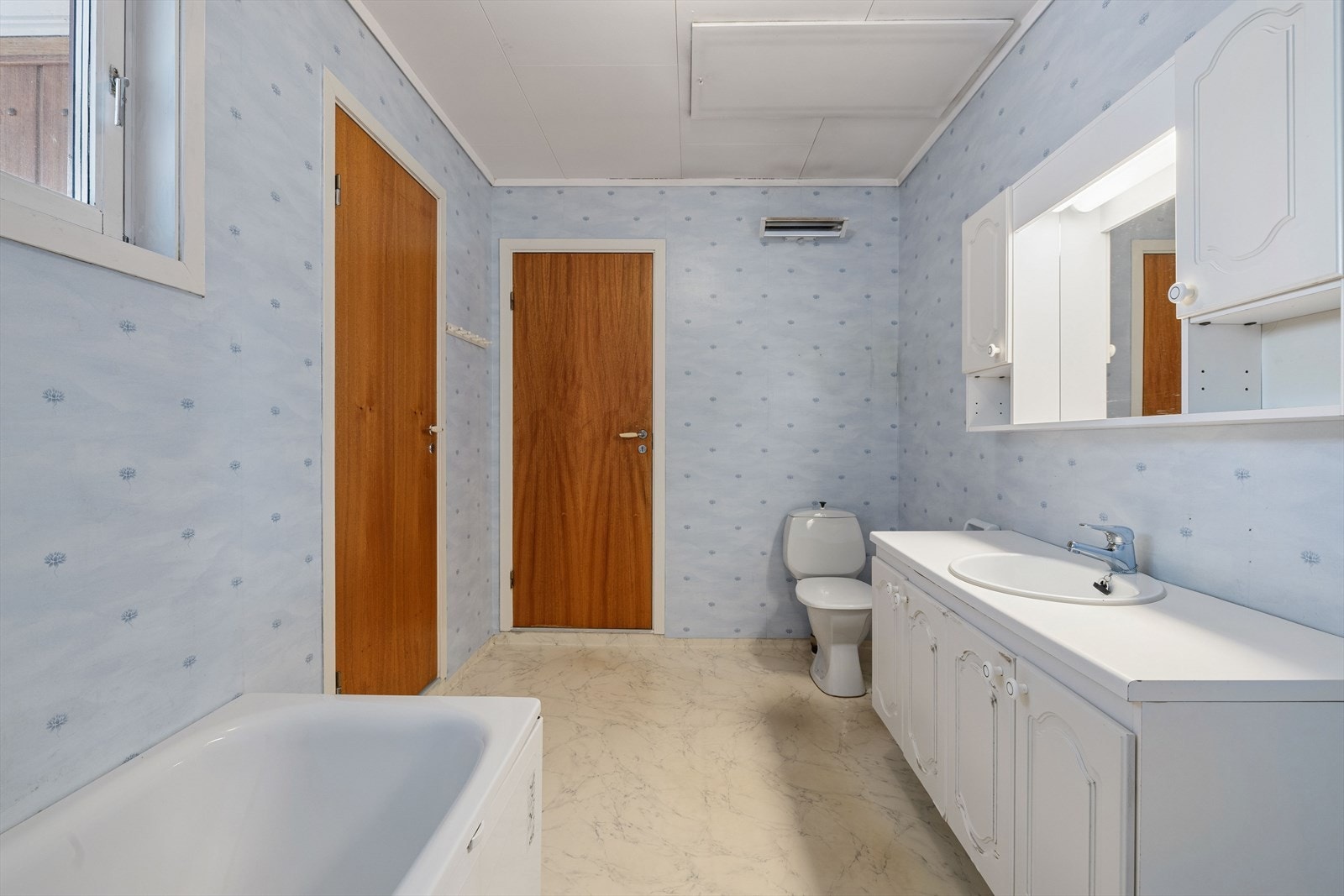 Belegg på gulvet og plater kledd med tapet på veggene. Det er adkomst til badet både fra entrèen og fra gangen. Galleribilde