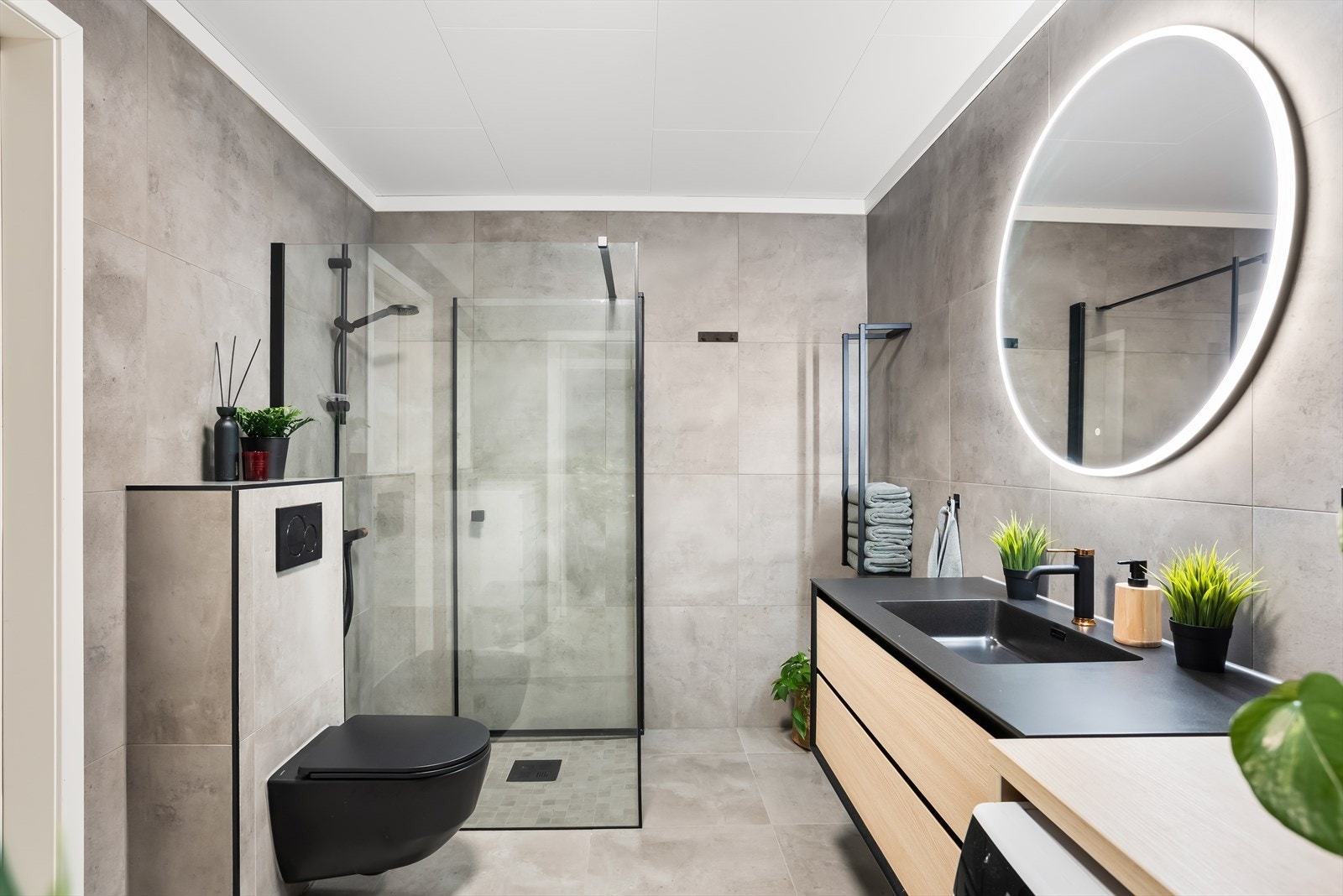 Badet har store 60x60 fliser, gulvvarme, innebygd sisterne og et dusjhjørne med sorte detaljer. Galleribilde