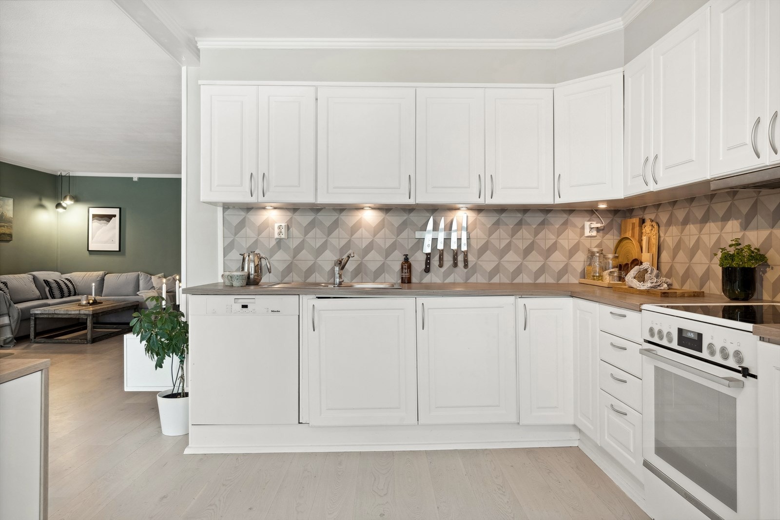 Kjøkkenet har innredning med lysmalte profilerte fronter, laminert benkeplate med nedfelt kjøkkenvask og vinyl på vegg over benk Galleribilde