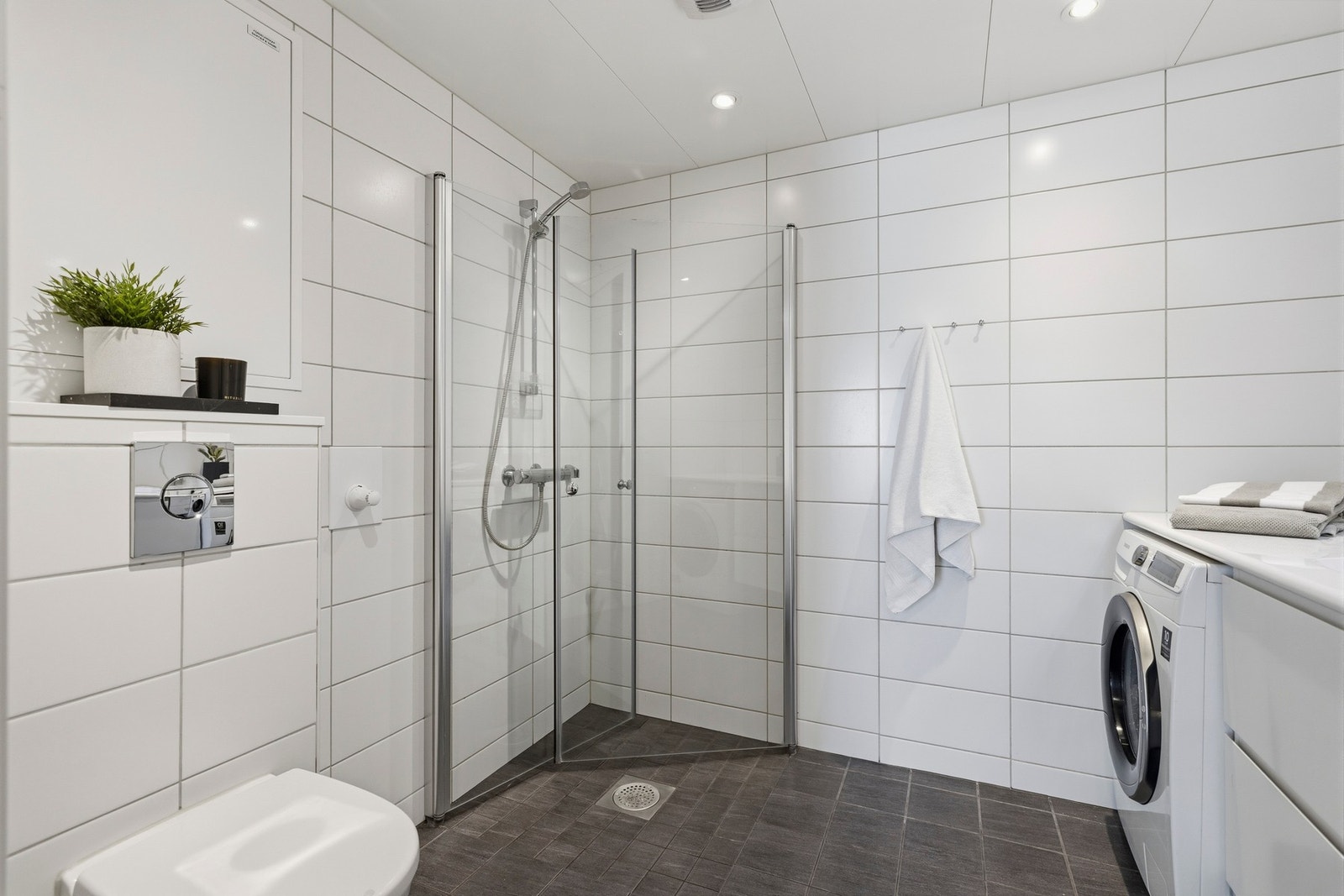 Badet er innredet med dusjhjørne med to svingbare glassdører, vegghengt toalett og en stilren baderomsinnredning med heldekkende servant. Galleribilde