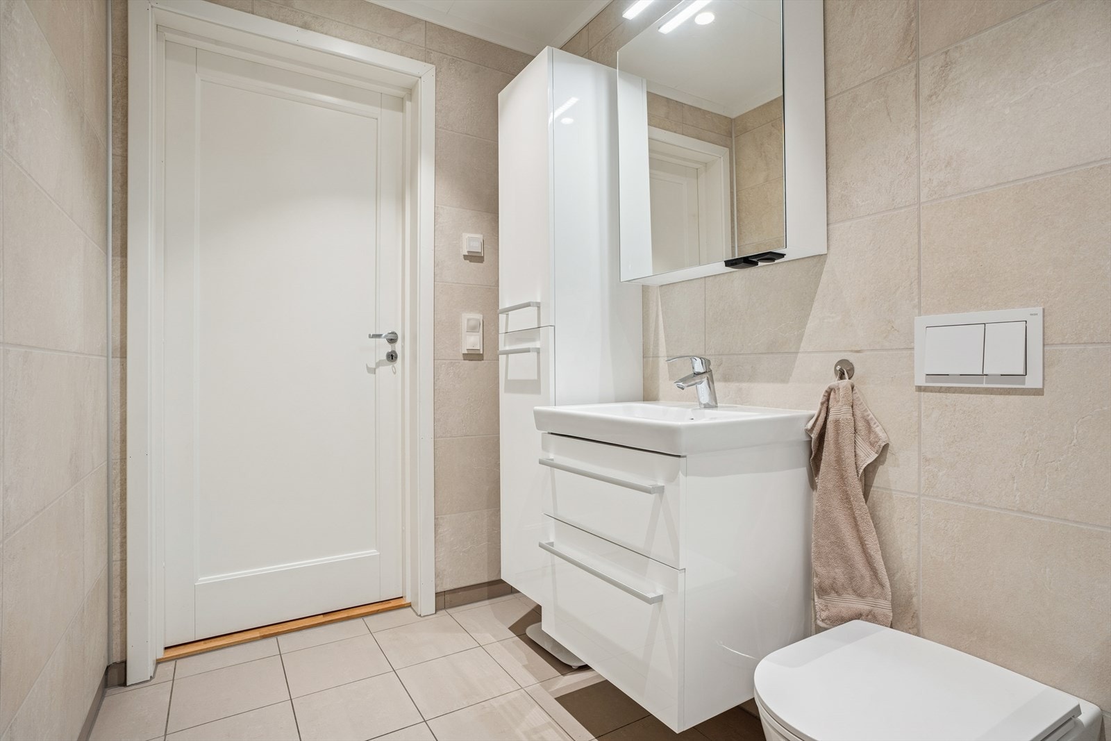 Innredningen består av heldekkende servant på skuffeseksjon, speilskap, dusjvegger og vegghengt toalett. Opplegg til vaskemaskin. Galleribilde