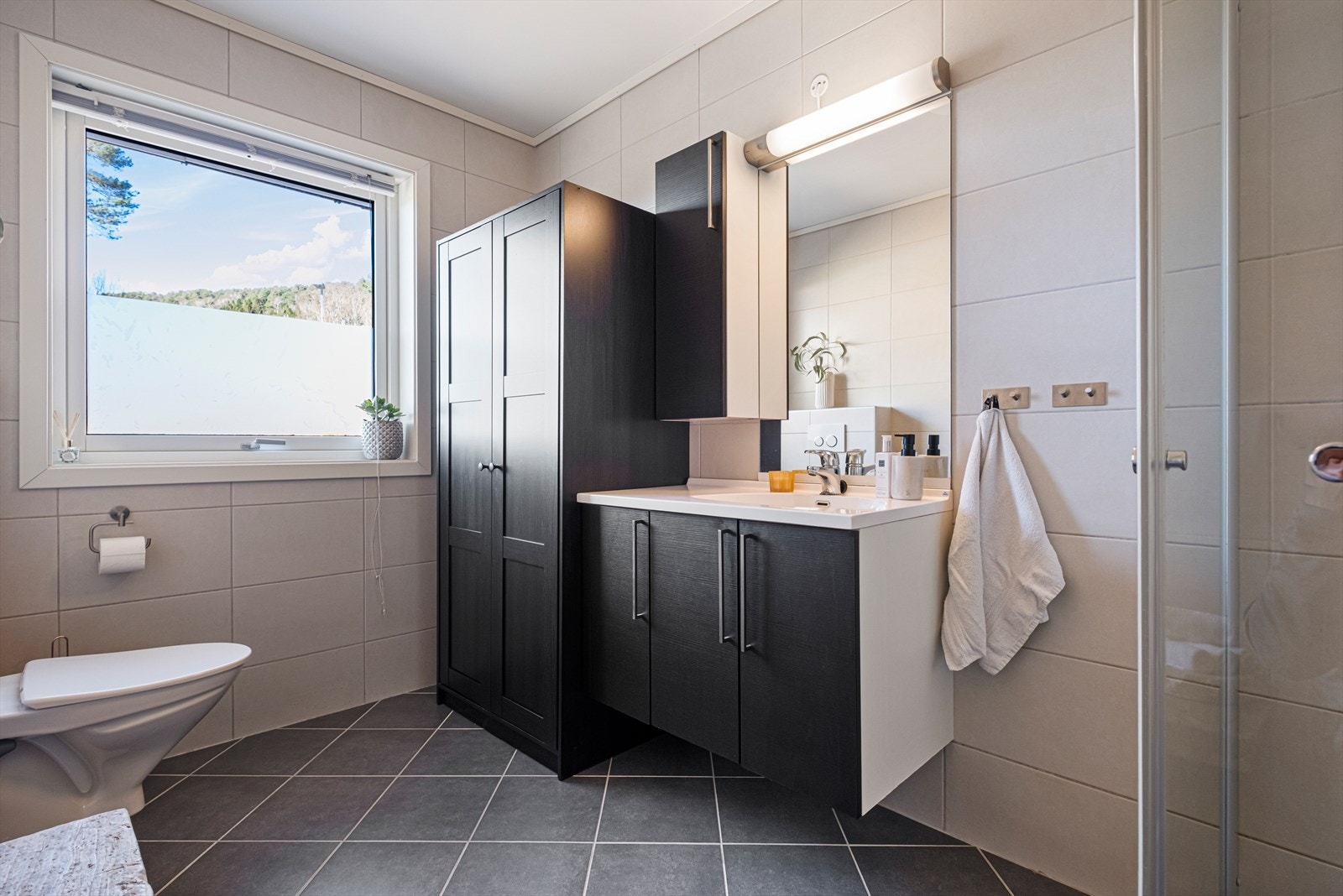 Innredningen inkluderer servant med mørke fronter, speil med belysning og vegghengt toalett. Galleribilde