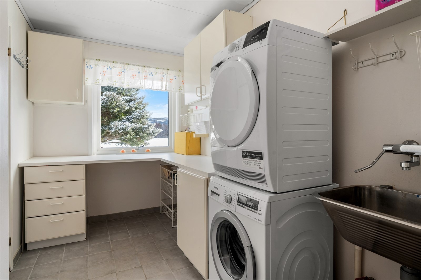 Vegg i vegg med badet er det etablert praktisk vaskerom på 6 m². Rommet er innredet med fliser på gulv, utslagsvask og opplegg for vaskemaskin. Galleribilde