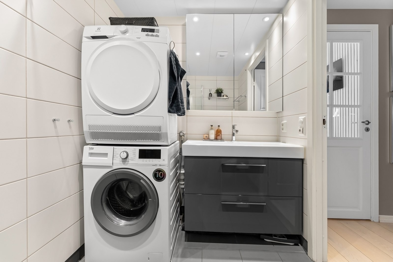 Badet er utstyrt med dusjhjørne med innfellbare dusjdører, regndusj og hånddusj fra Grohe, veggmontert toalett, baderomsinnredning med skuffer, servant med blandebatteri fra Grohe og vegghengt speilskap. Galleribilde