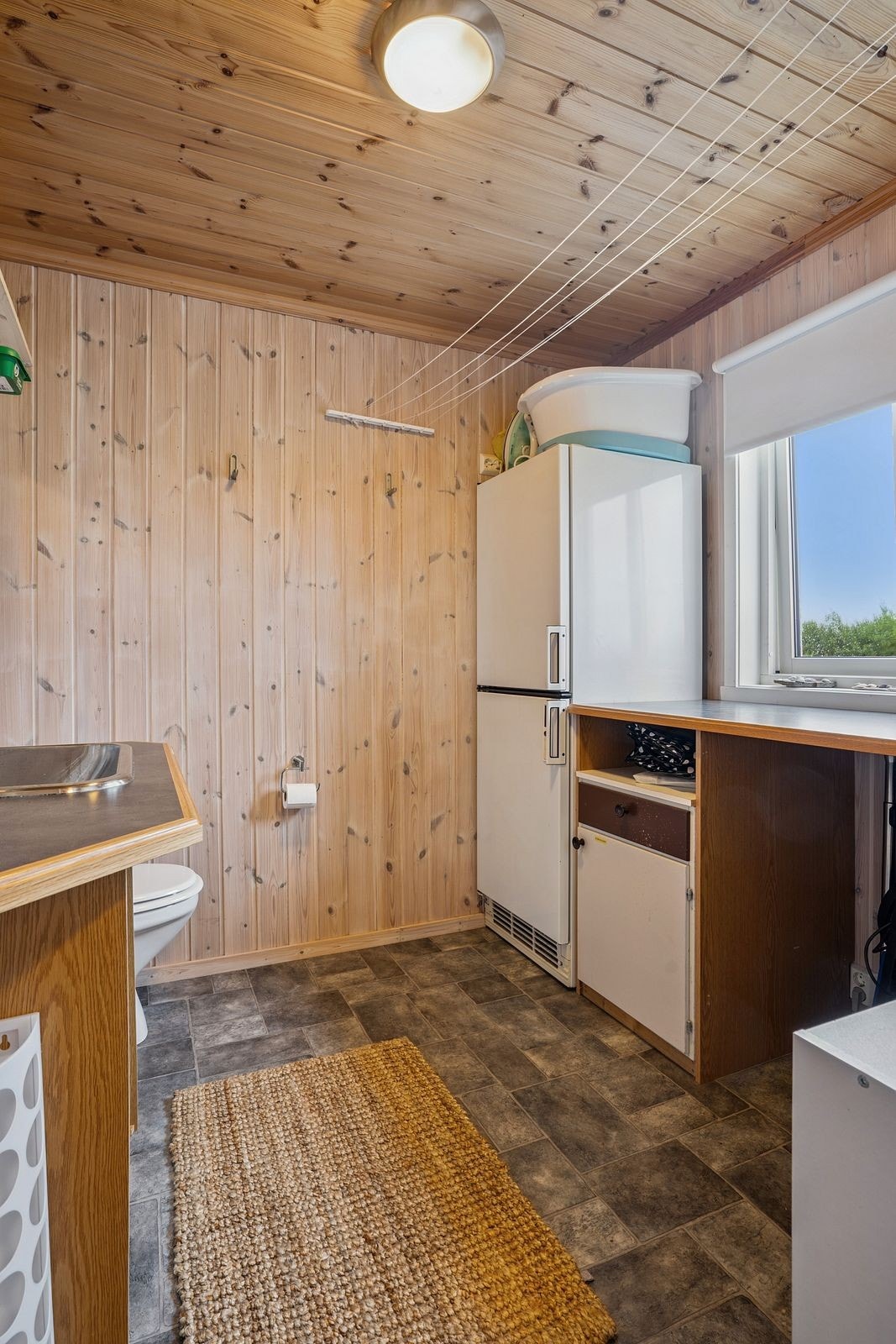 Innvendig bod med toalett er innredet med benkeplate og servant, vegghengt blandebatteri og toalett. Kjøleskap følger med. Galleribilde