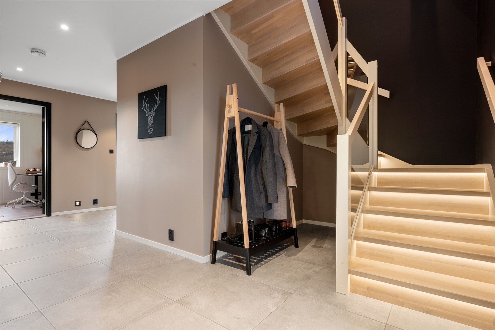 Stor gang/hall med store fine fliser på gulv. Integrert belysning i trapp med glassrekkverk. Galleribilde