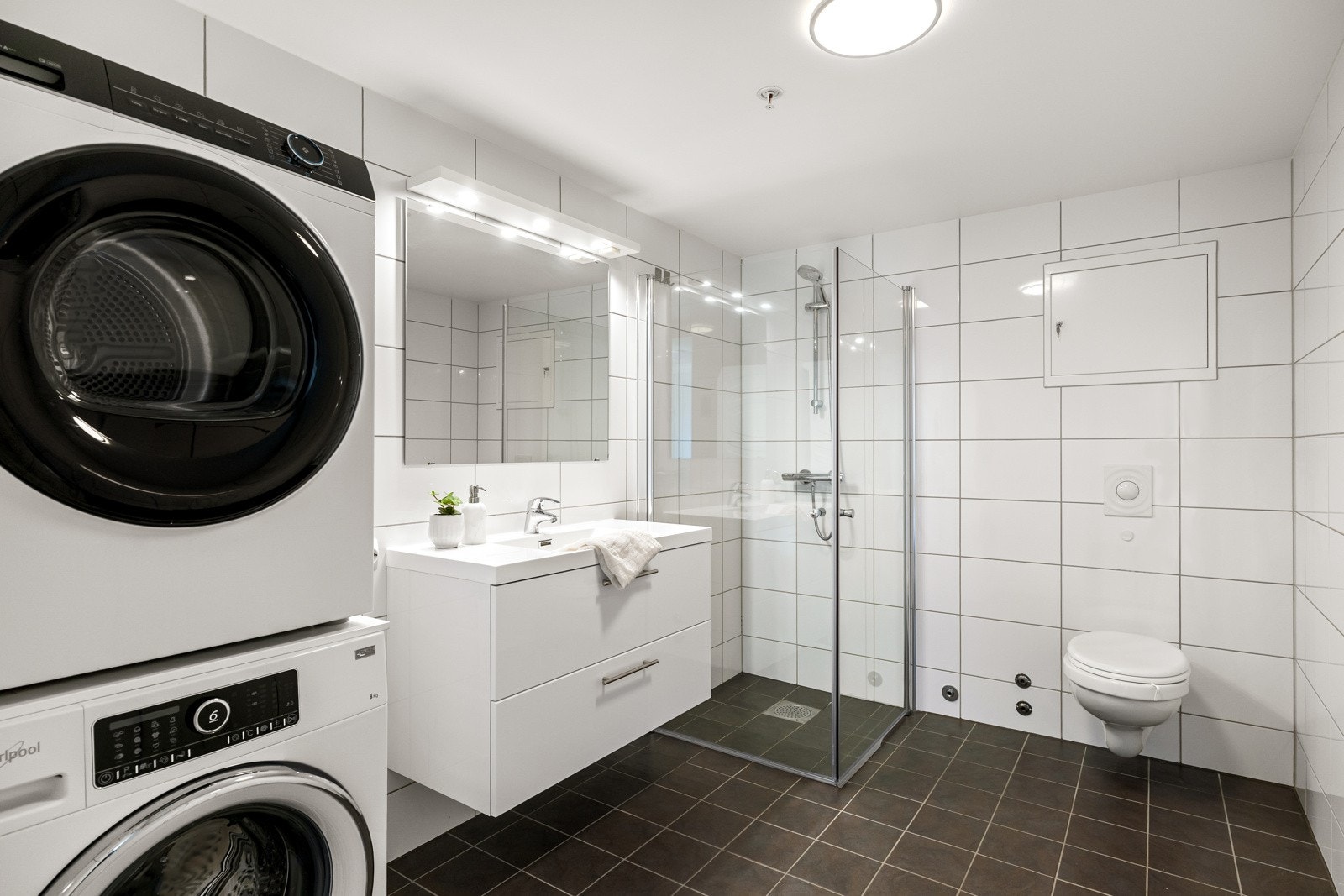 Badet fremstår som velholdt og moderne, med hvite fliser på veggene og koksgrå fliser på gulv med gulvvarme Galleribilde