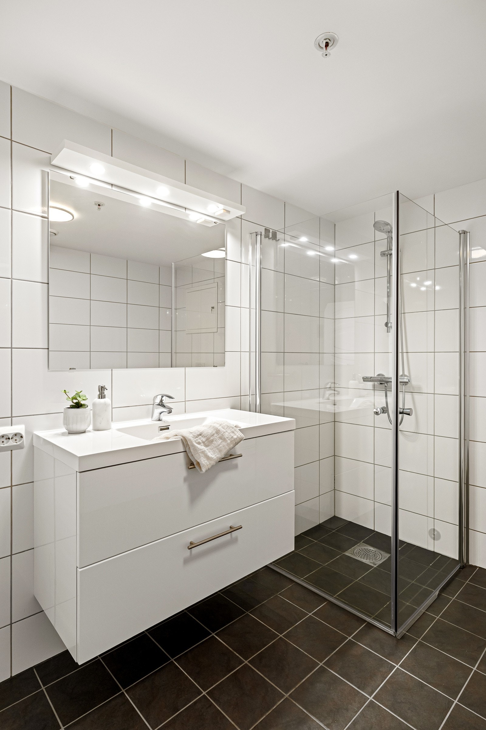 Baderomsinnredningen fra 2025 har hvite fronter og består av en heldekkende servant på en skuffeseksjon og et stort speil med god belysning Galleribilde