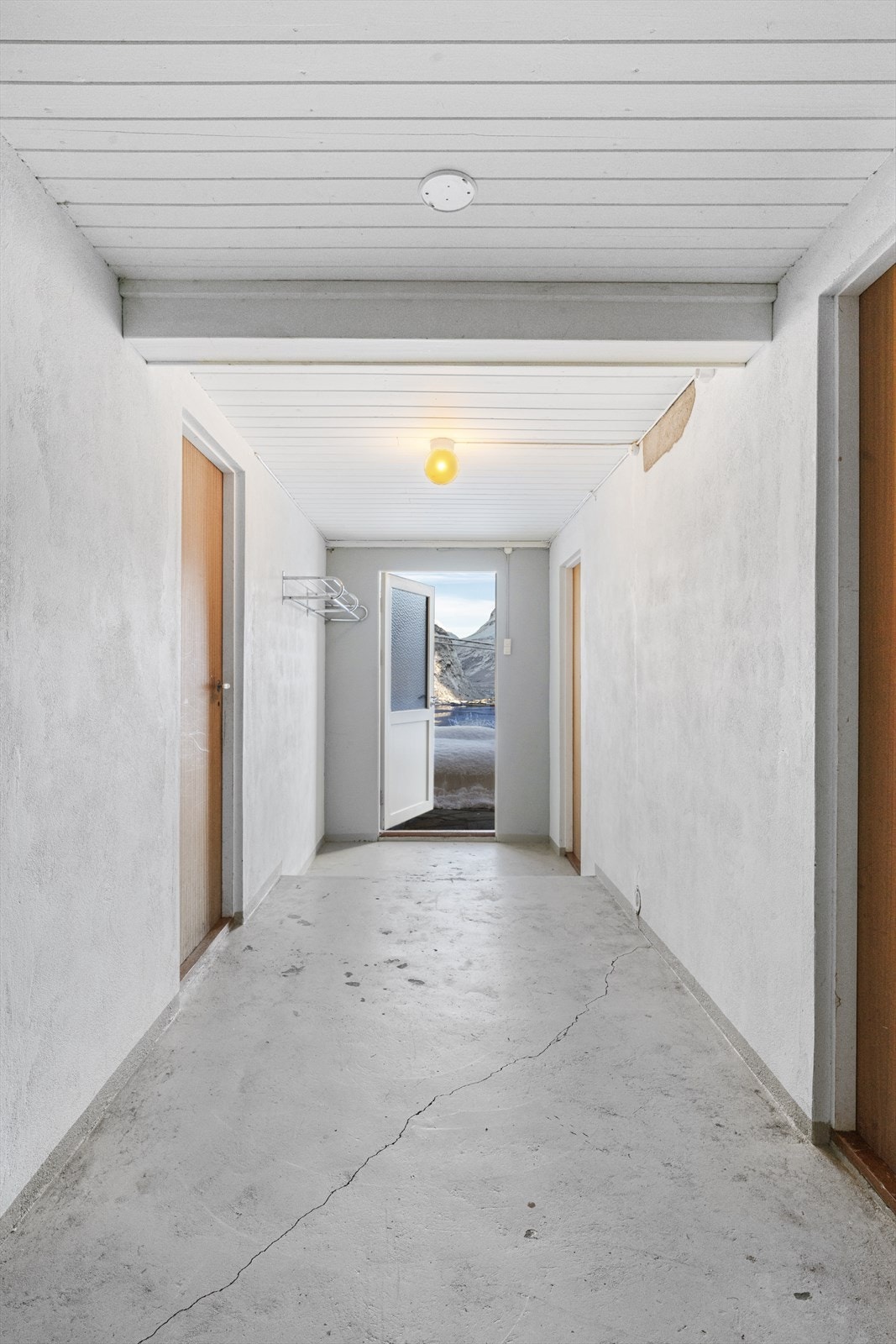 Betonggulv og malte murvegger i gangen i underetasjen, og dør direkte ut til hagen. Galleribilde
