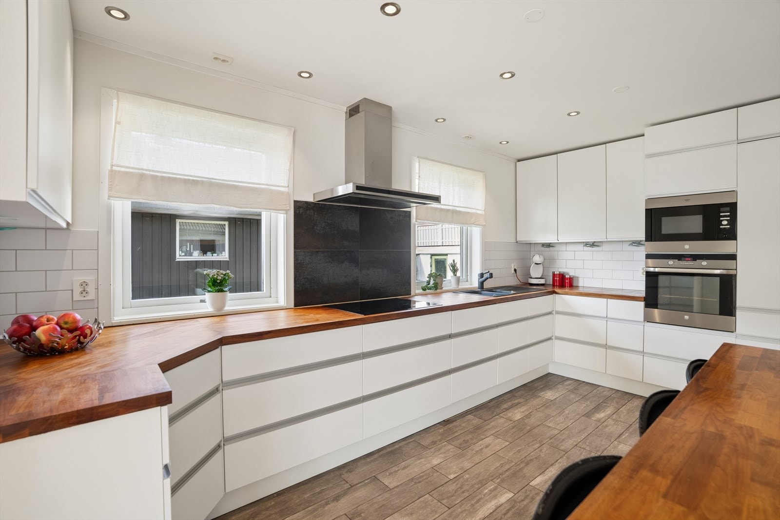 Benkeplaten i heltre eik gir en varm kontrast til de slette, hvite frontene. Kjøkkenventilator med avtrekk ut. Galleribilde