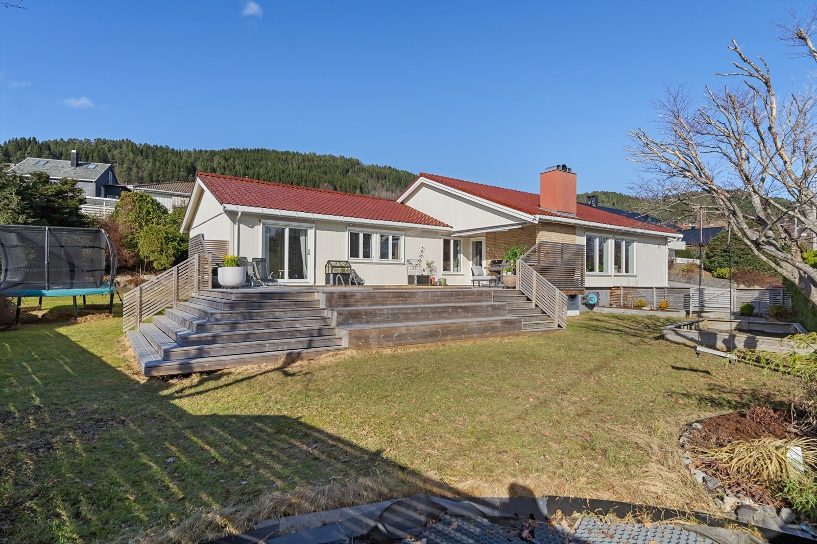 Eiendommen strekker seg over en flat, opparbeidet tomt med stor plen og en imponerende trappeterrasse ned fra boligens hovedplan. Galleribilde