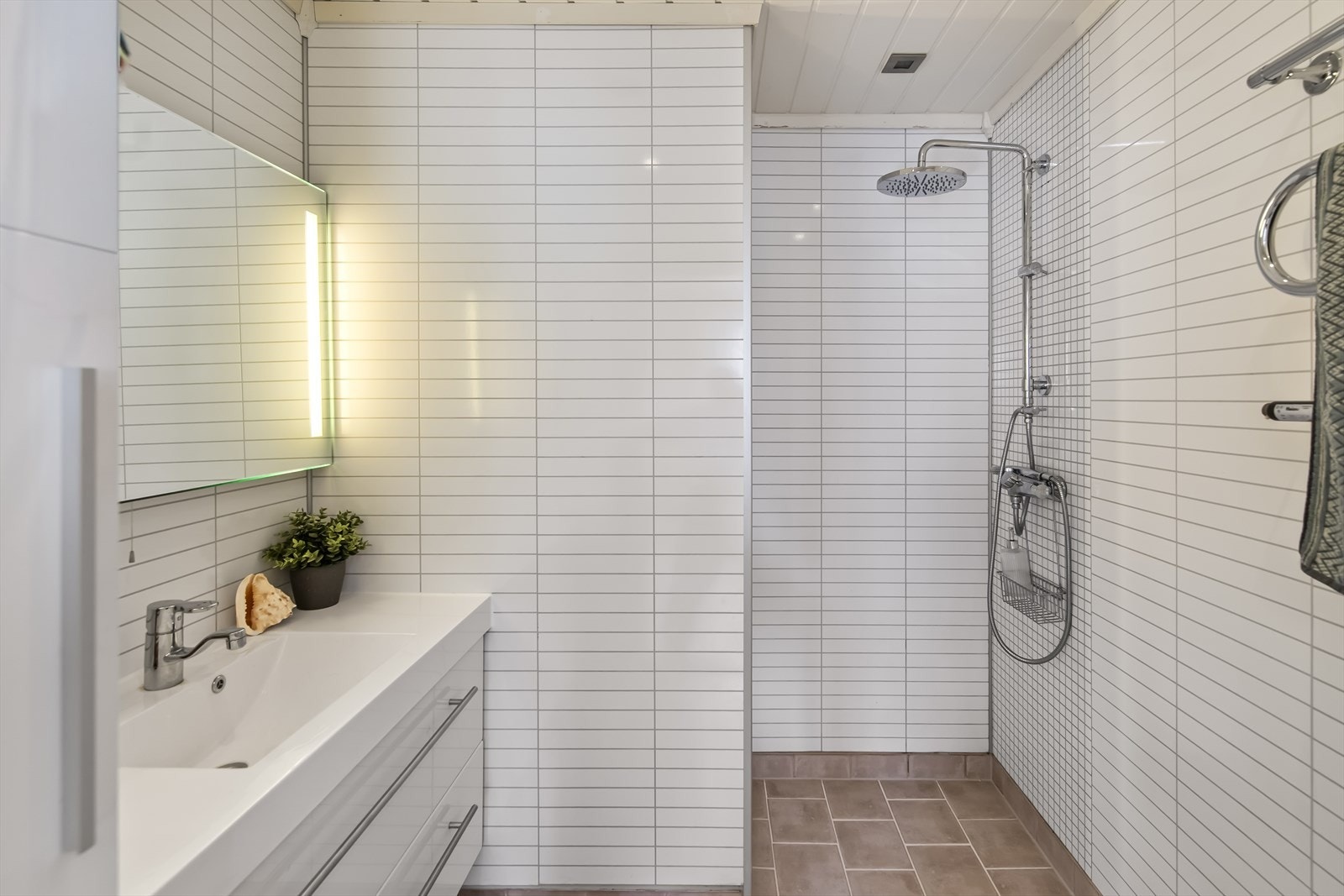 Dette badet er tilknyttet hovedsoverommet, utstyrt med baderomsplater på vegger, flislagt gulv med varmekabler, veggmontert toalett og dusjhjørne. Galleribilde