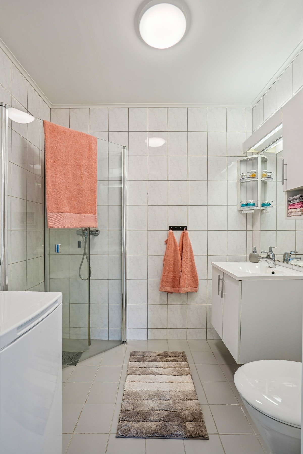 Flislagt bad fra byggeår, med hengslede dusjvegger i glass og opplegg for vaskemaskin. Galleribilde