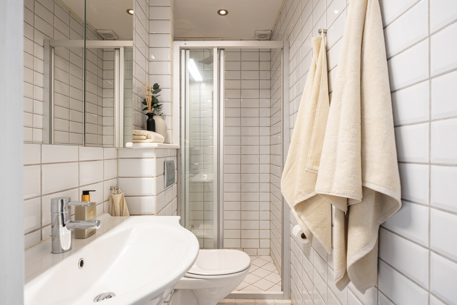 Lyst og pent flislagt bad med dusjhjørne med skyvedører Galleribilde