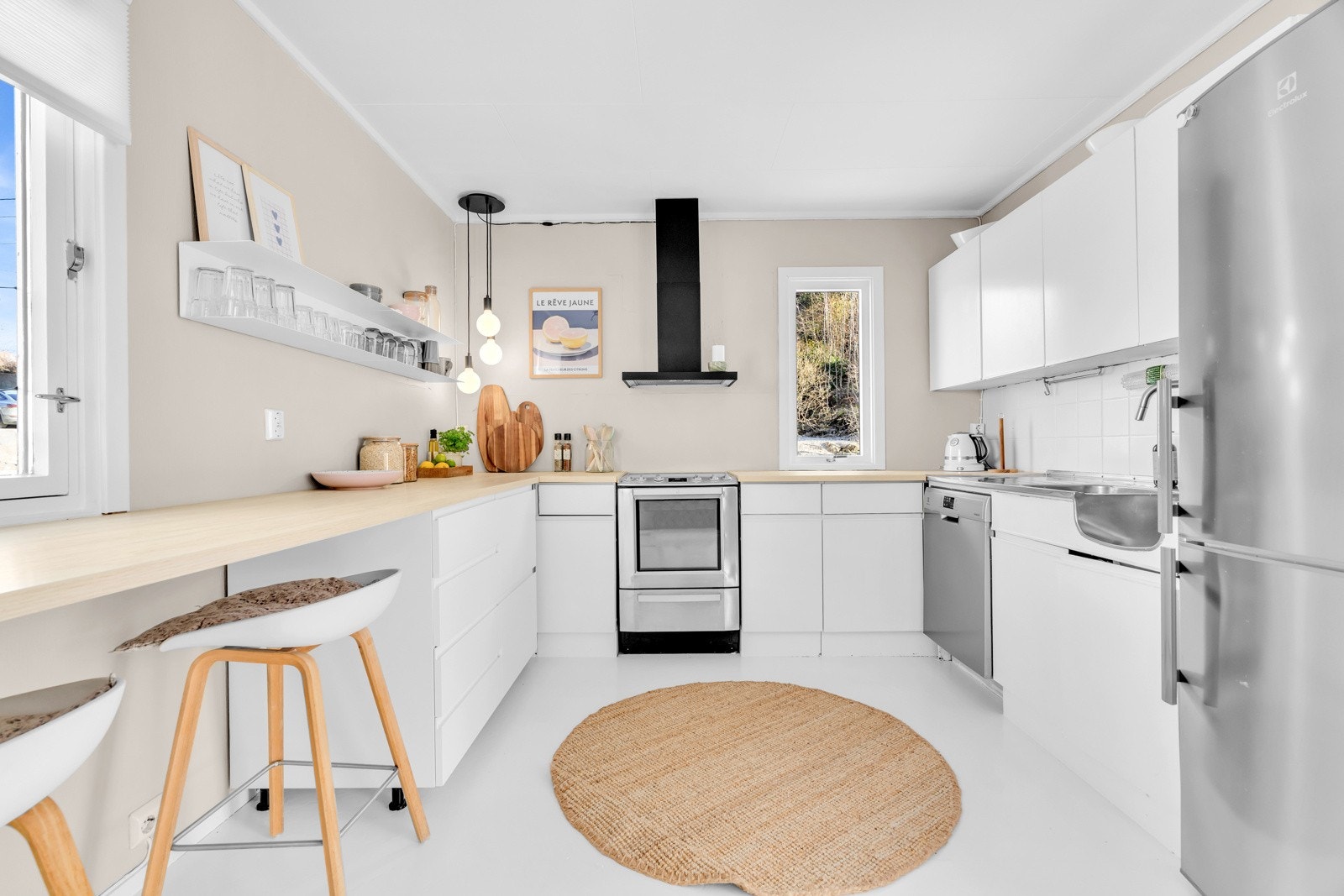 Kjøkkenet er stilrent med hvite fronter og lys benkeplate Galleribilde