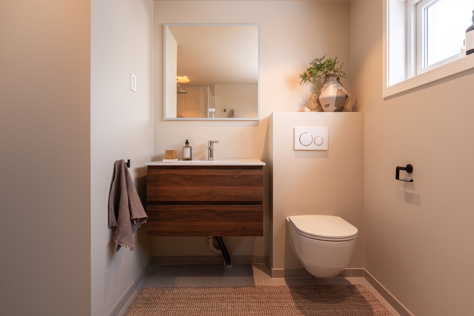 Innredningen består av veggmontert toalett, servant på nøttebrun skuffeseksjon og speil. Galleribilde