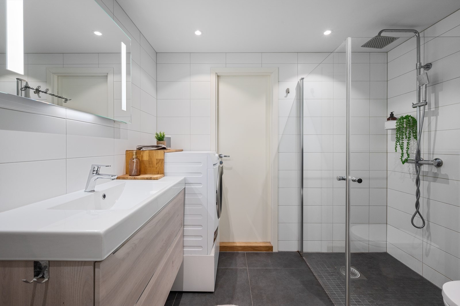 Badet er innredet med nedfelt servant, veggmontert toalett, dusjhjørne med innfellbare glassvegger og opplegg for vaskemaskin. Galleribilde