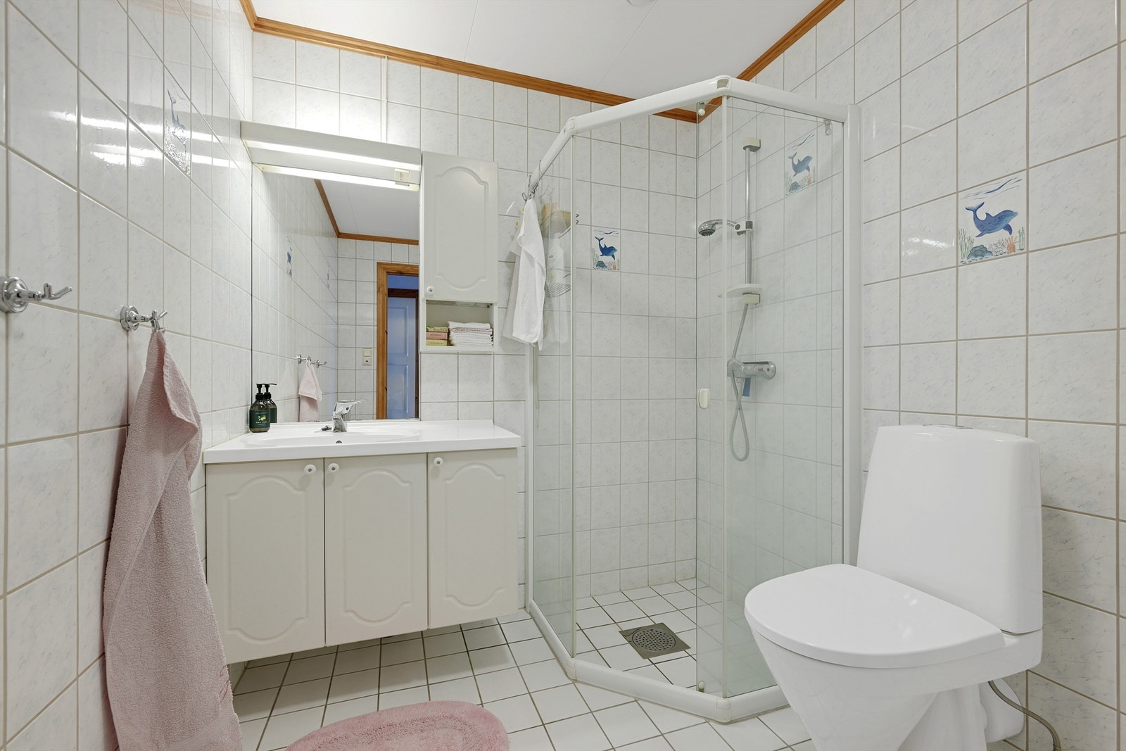 Flislagt badeværelse med dusjhjørne, håndvask i innredning med speil og overskap, wc og plass/opplegg for vaskemaskin Galleribilde