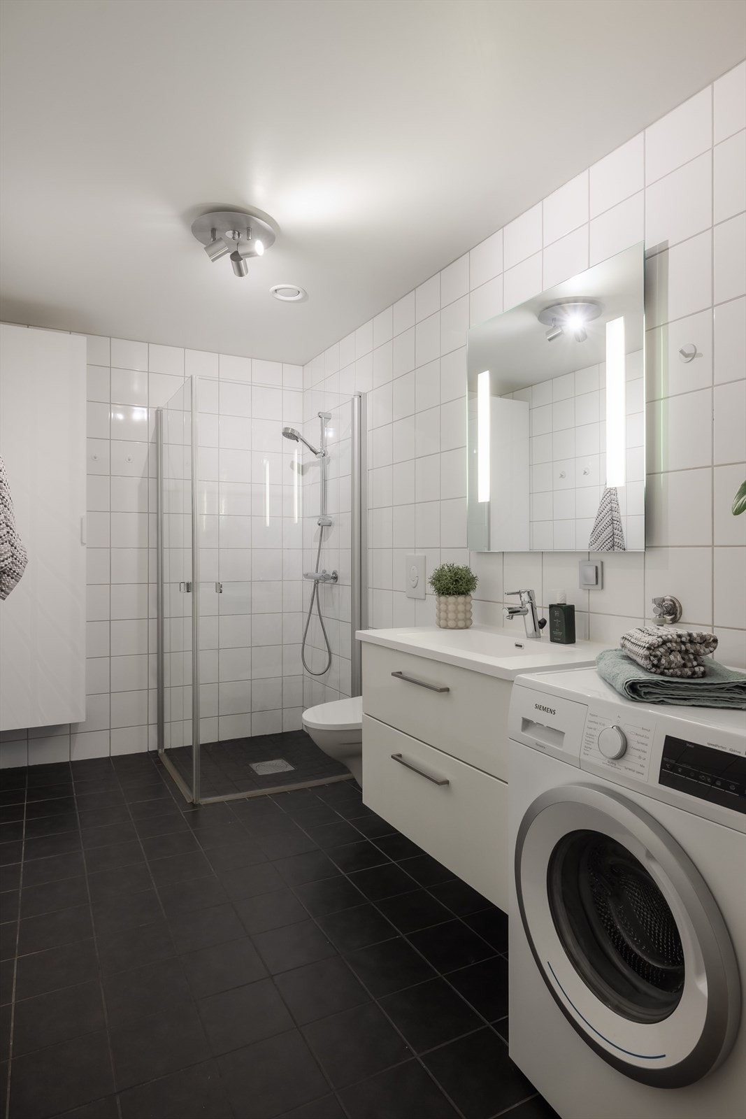 I tillegg har badet veggmontert toalett og dusjhjørne med innfellbare dusjdører og vegghengt dusjbatteri. Det er et ekstra skap på veggen. Galleribilde