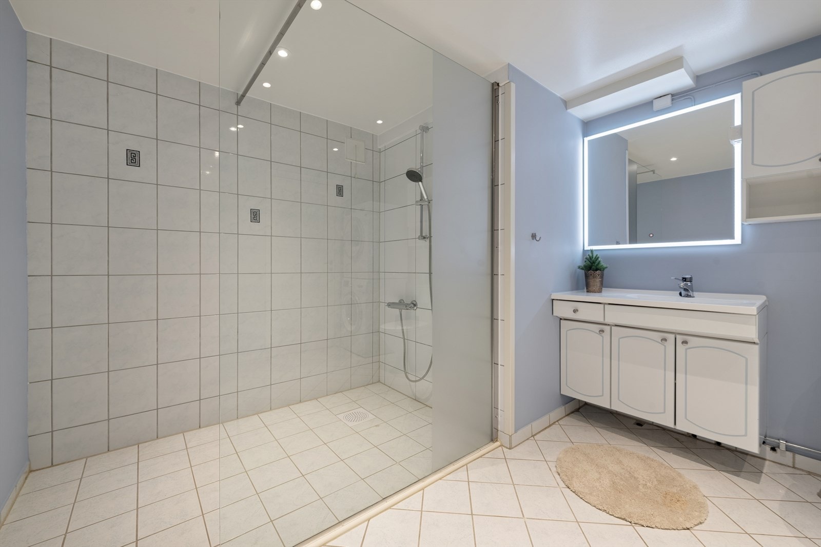 Badet har flislagt gulv med gulvvarme, malte og flislagte vegger, samt himling med malt, slett overflate og downlights. Det er vegghengt servantskap med heldekkende servant og ett-greps armatur. Galleribilde
