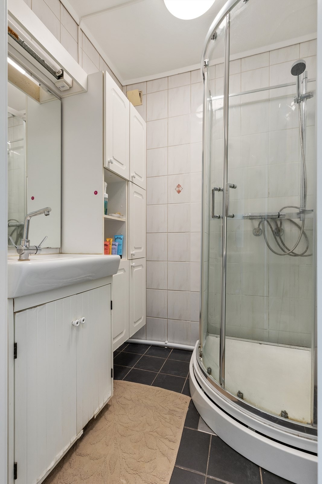 Flislagt baderom med underliggende elektrisk gulvvarme, innredet med skap med slette fronter samt servant og dusjkabinett Galleribilde